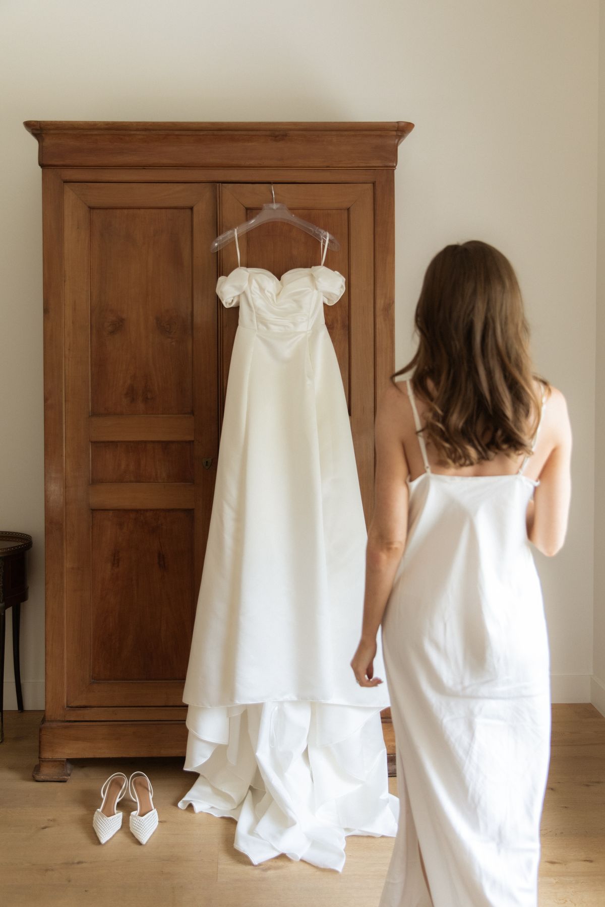 Bride with hanging wedding gown in the prep suite at Chateau Gassies, Nouvelle-Aquitaine