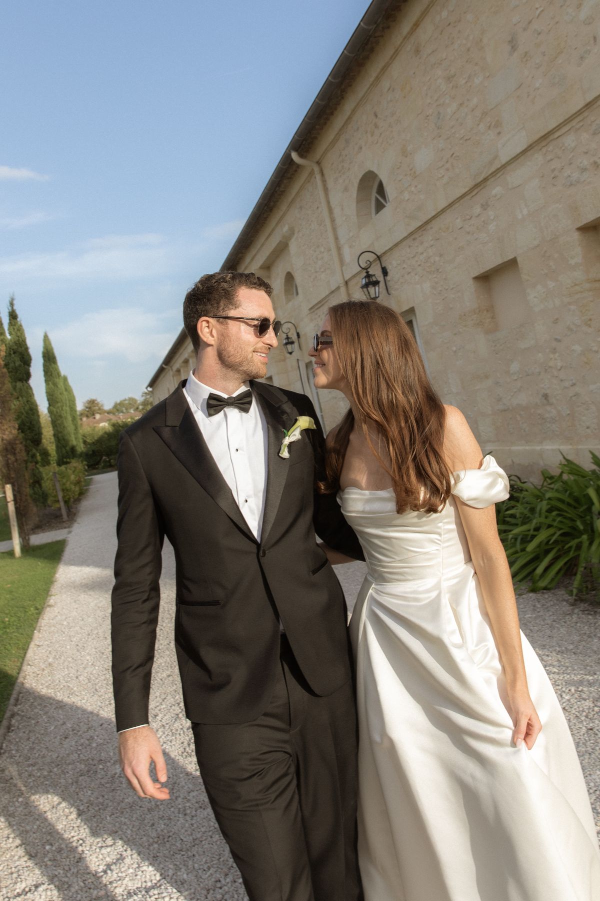 Bride and groom in sunglasses walking by the chateau at Chateau Gassies, Nouvelle-Aquitaine