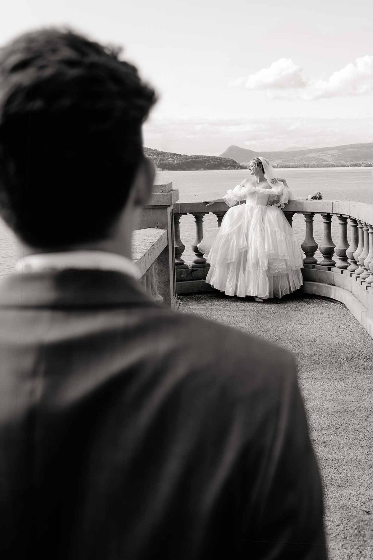 Groom watching bride at lake terrace balustrade in black and white at Palace de Menthon