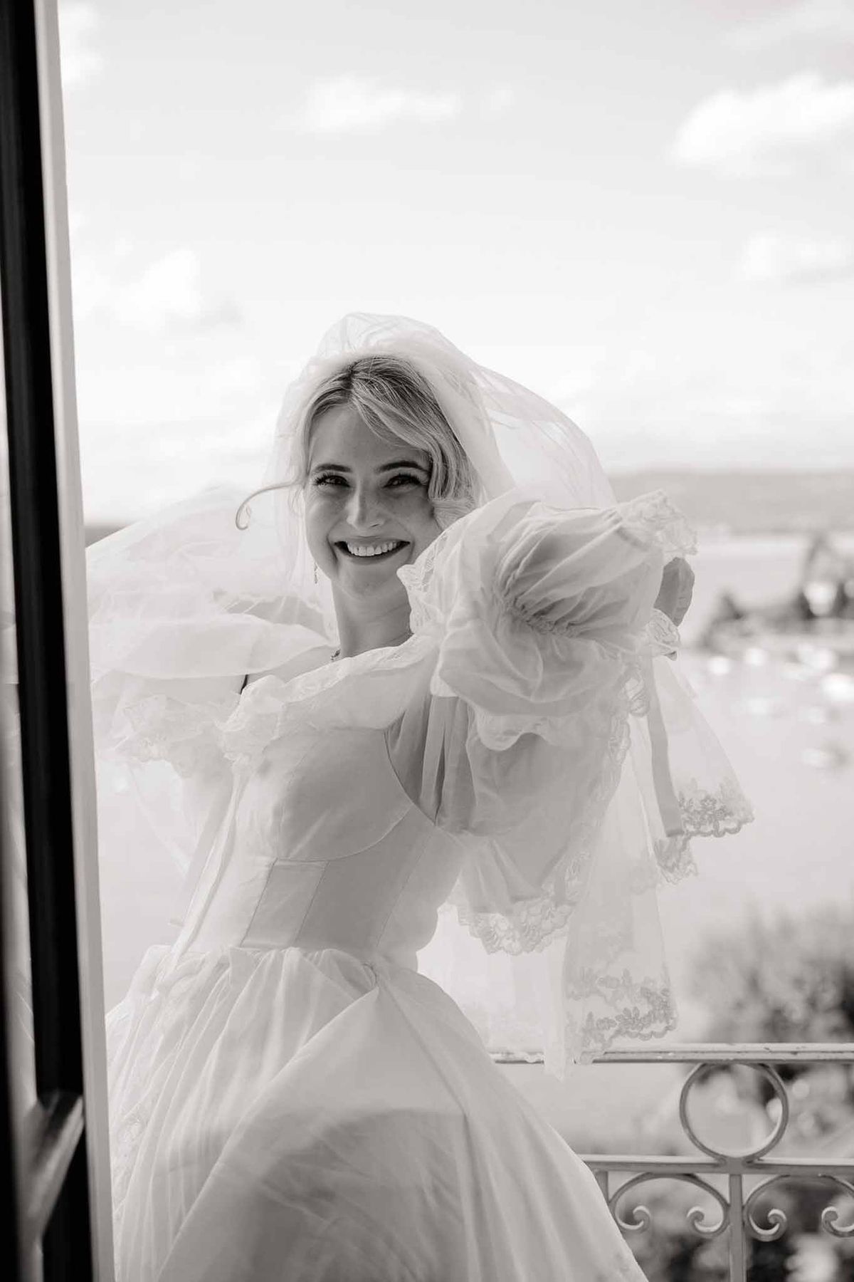Bride smiling in vintage gown on balcony in black and white at Palace de Menthon Annecy