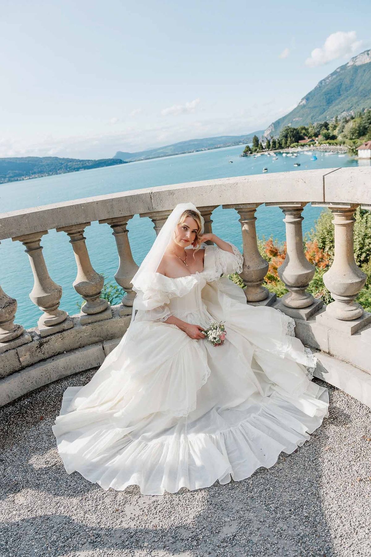 Bride in vintage ball gown sitting on terrace with Lake Annecy views at Palace de Menthon