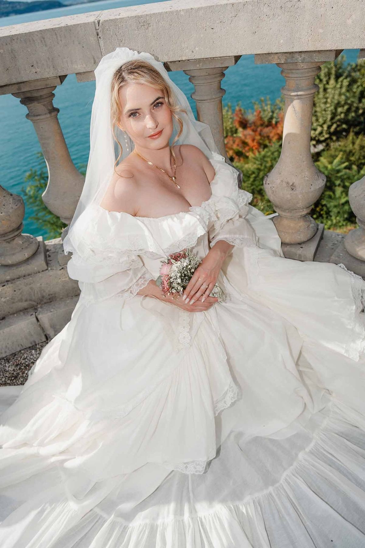 Bride in vintage gown with bouquet and Lake Annecy behind at Palace de Menthon