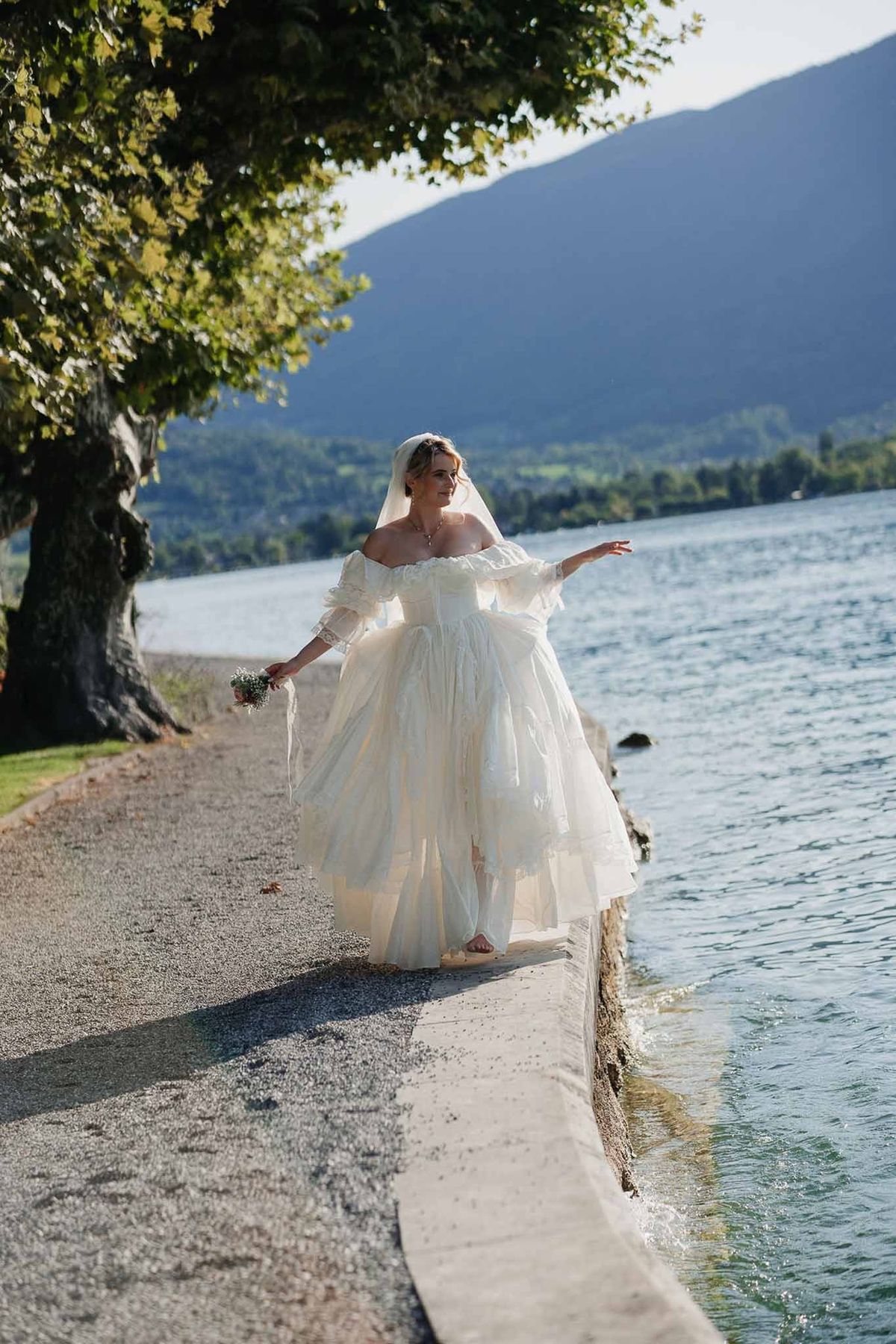 Bride walking along Lake Annecy shoreline in vintage gown at Palace de Menthon