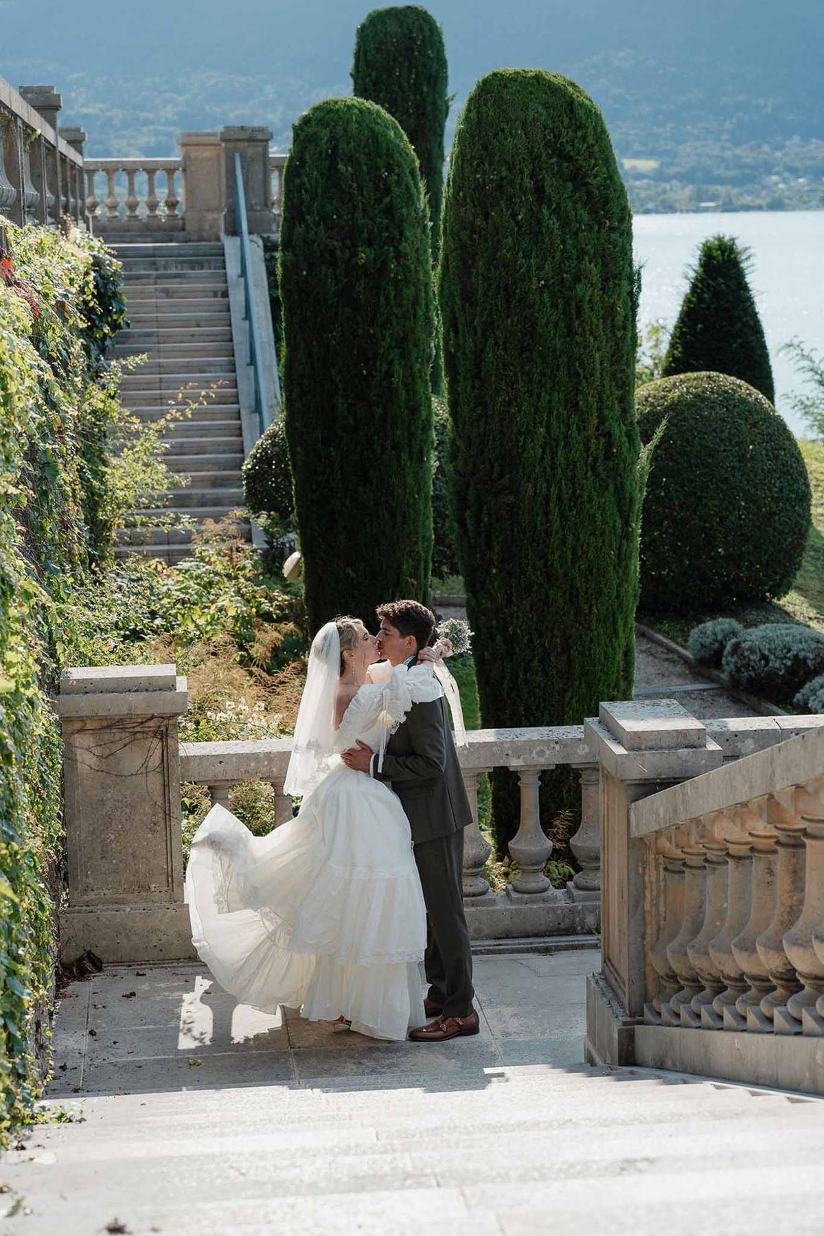 Couple kissing by cypresses on stone terrace with lake behind at Palace de Menthon