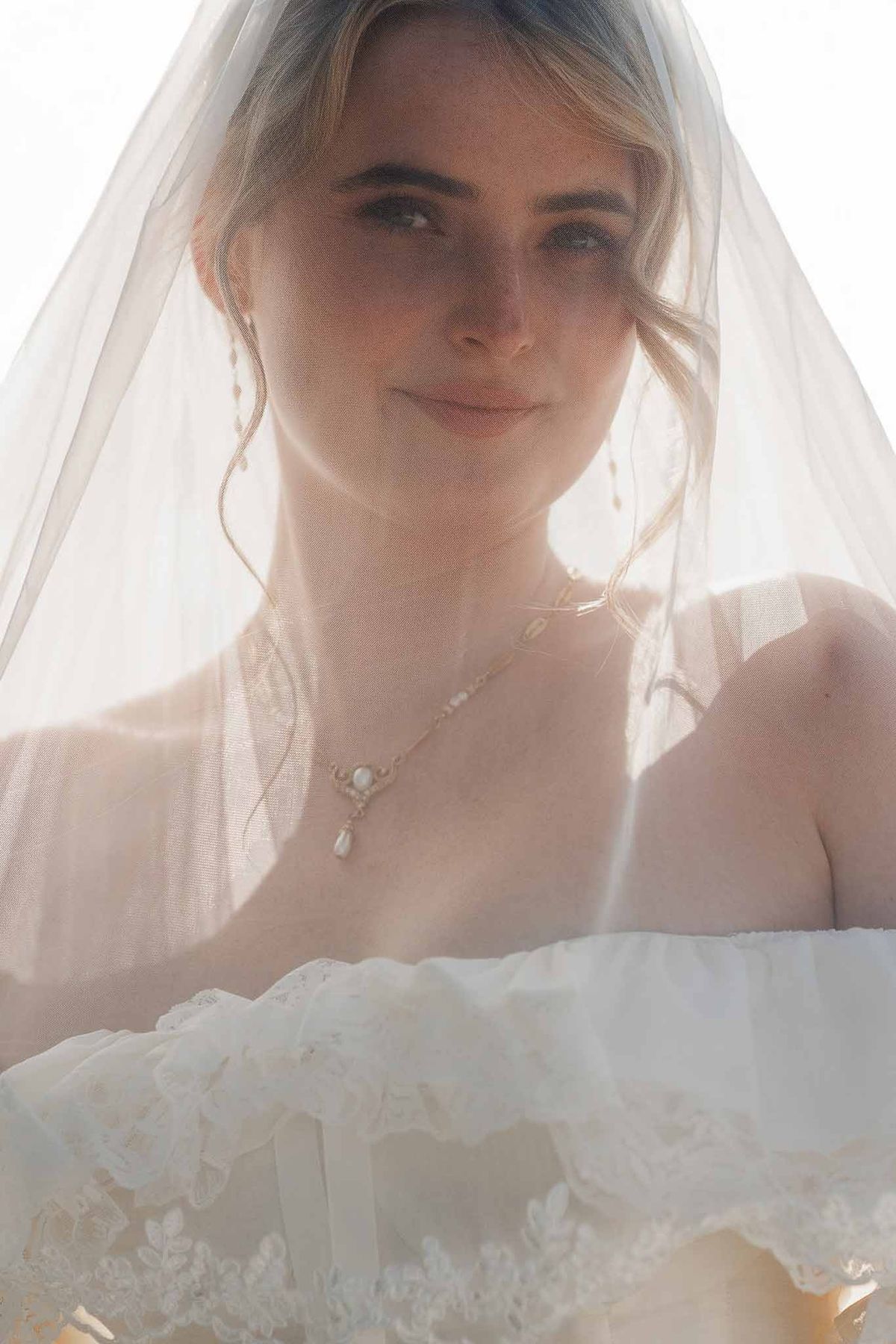 Bride smiling through veil with pearl necklace at golden hour at Palace de Menthon