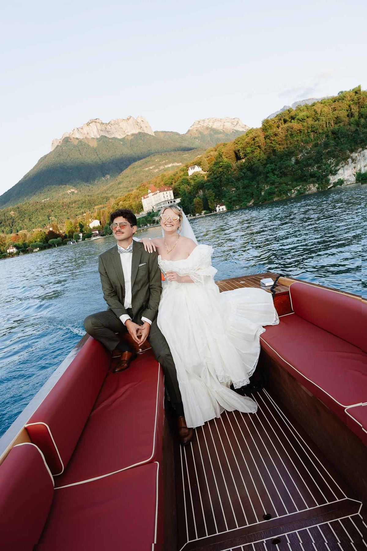 Couple on speedboat with Château de Menthon and mountains behind on Lake Annecy