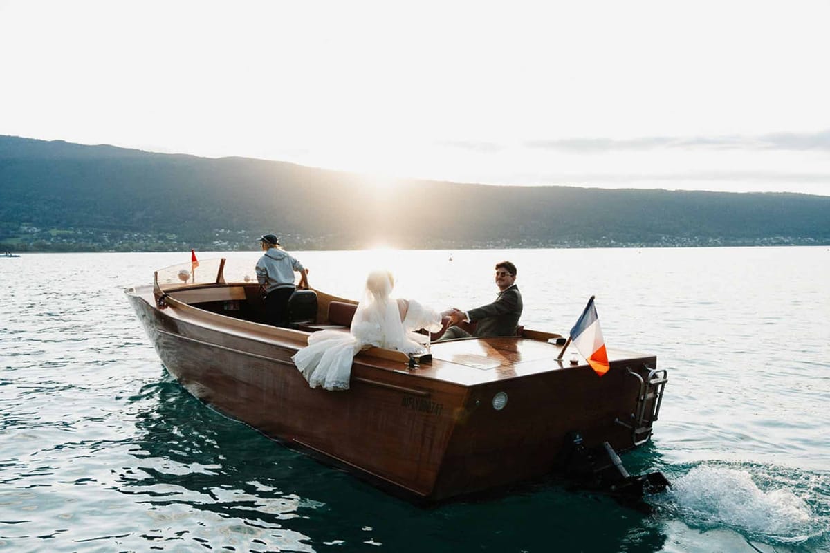 Couple departing on wooden boat with French flag at sunset on Lake Annecy at Palace de Menthon