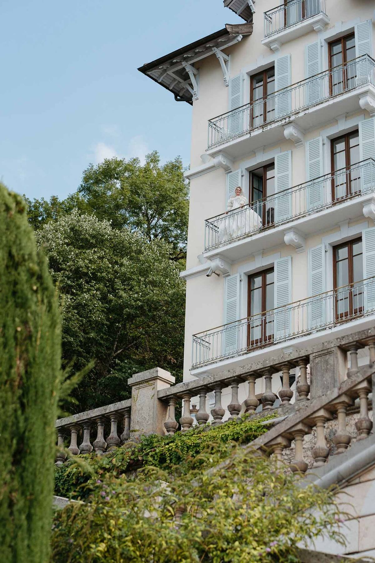 Bride on balcony of Belle Époque Palace de Menthon with cypress tree
