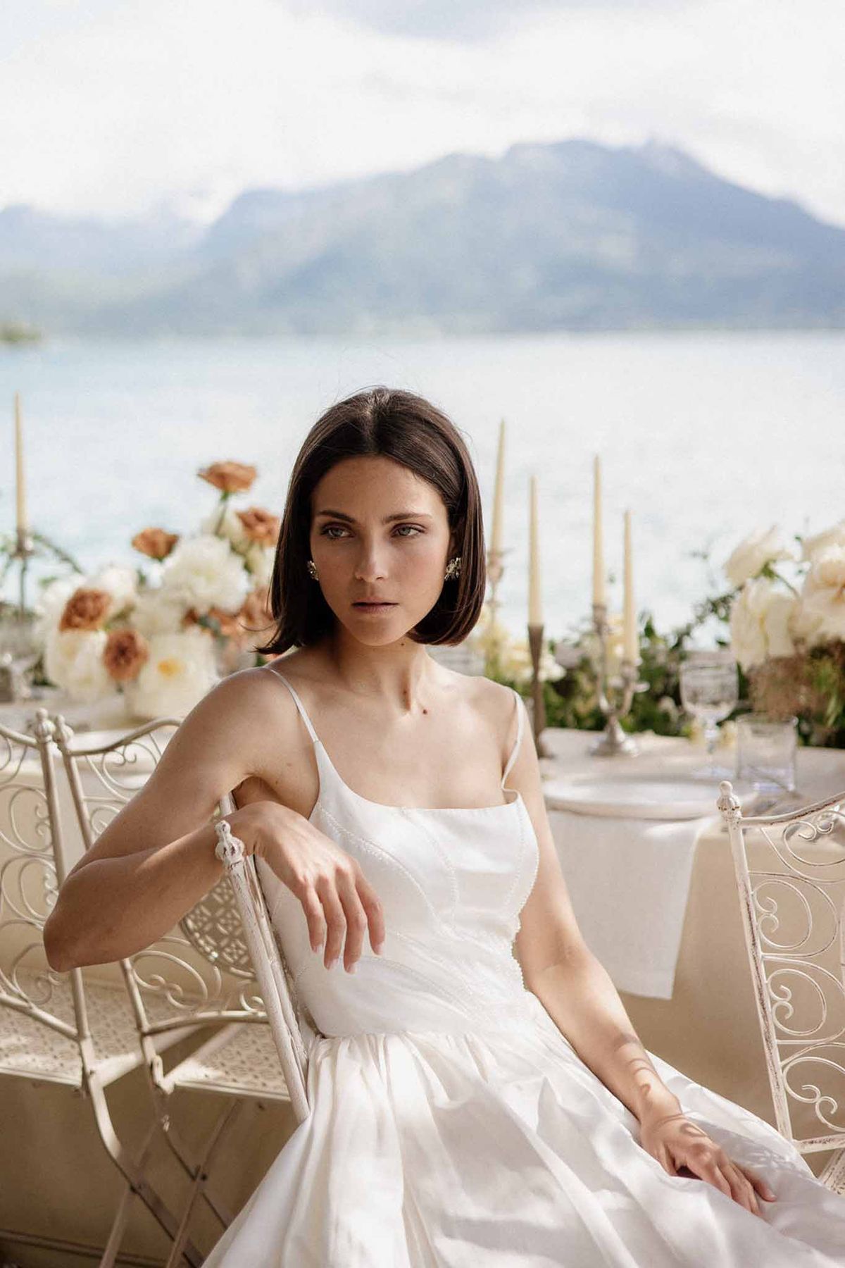 Bride seated on terrace with peony and terracotta rose tablescape overlooking lake and mountains behind