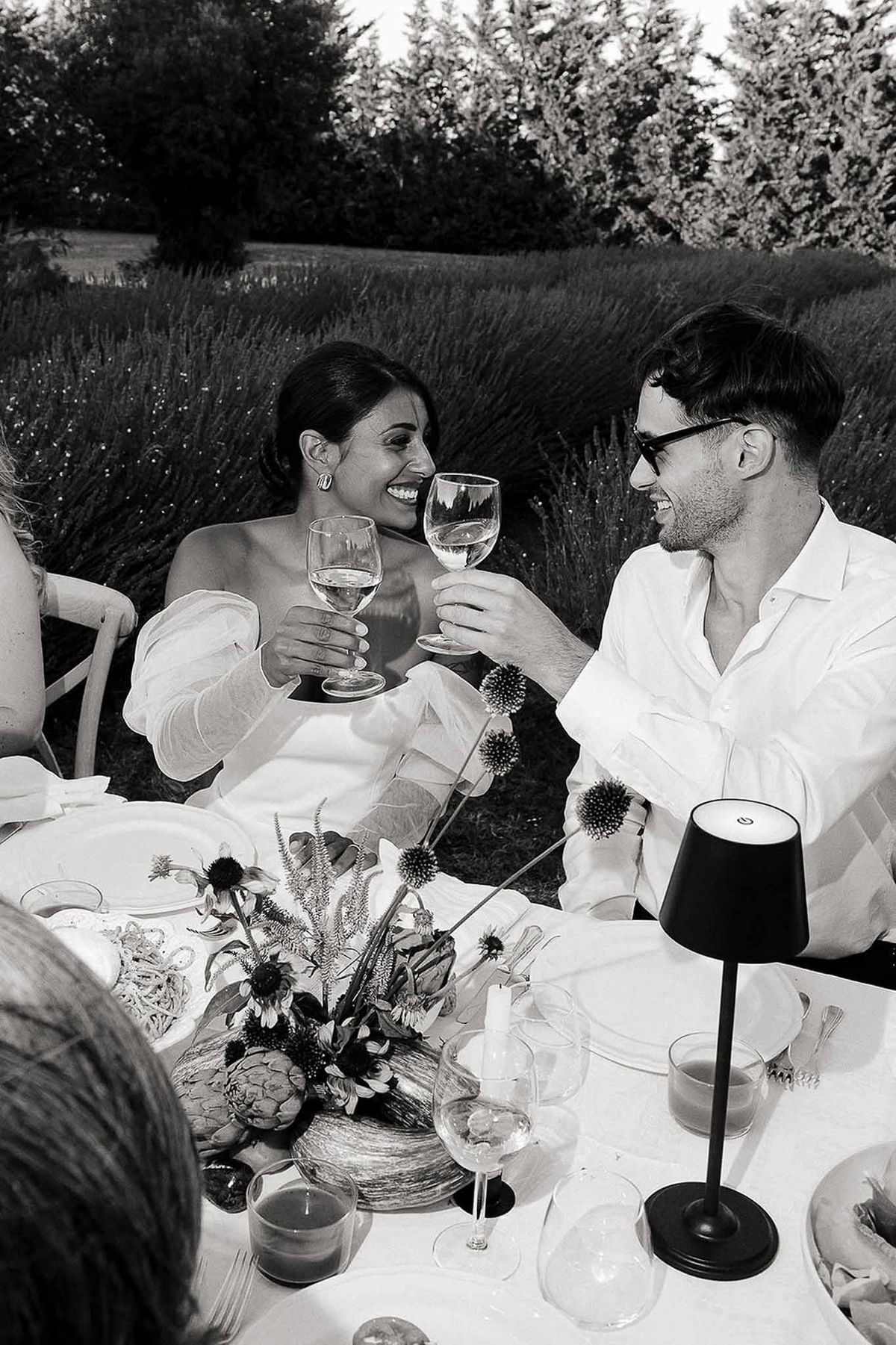 Bride and groom seated at reception table raising champagne glasses for a toast, Bastide des Barattes