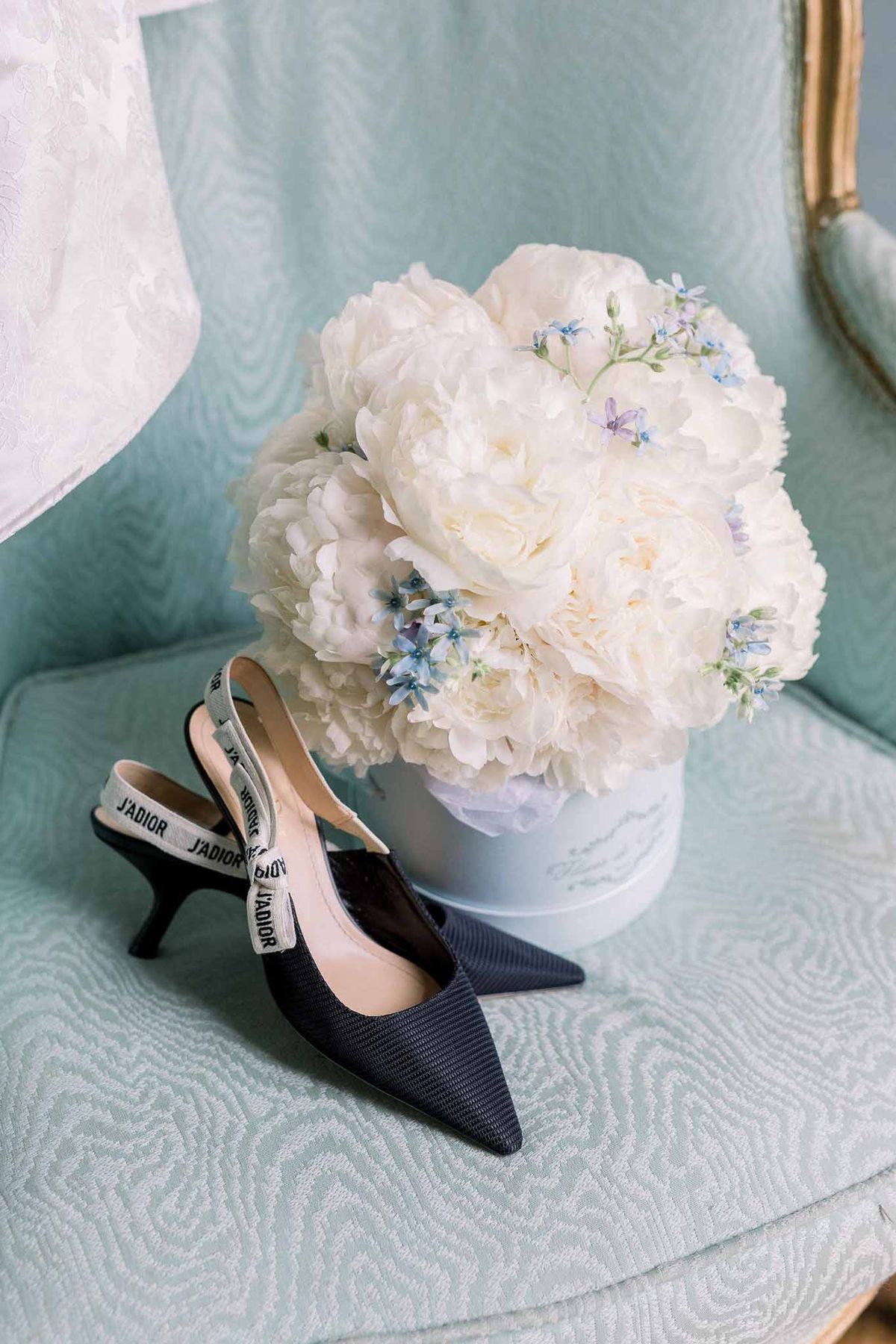 Navy Dior slingback heels on mint armchair with white peony and forget-me-not hatbox arrangement