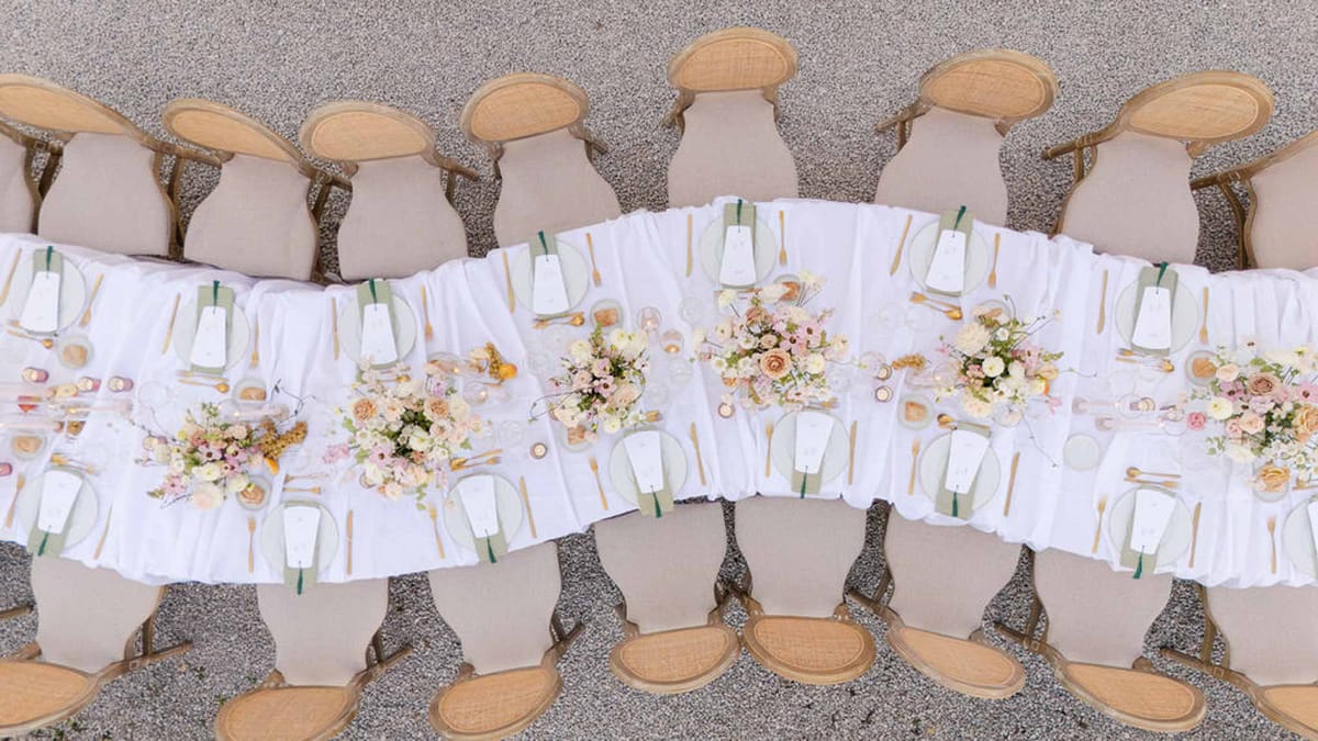 Aerial view of long table with sage napkins, gold flatware, and ivory and blush rose centrepieces