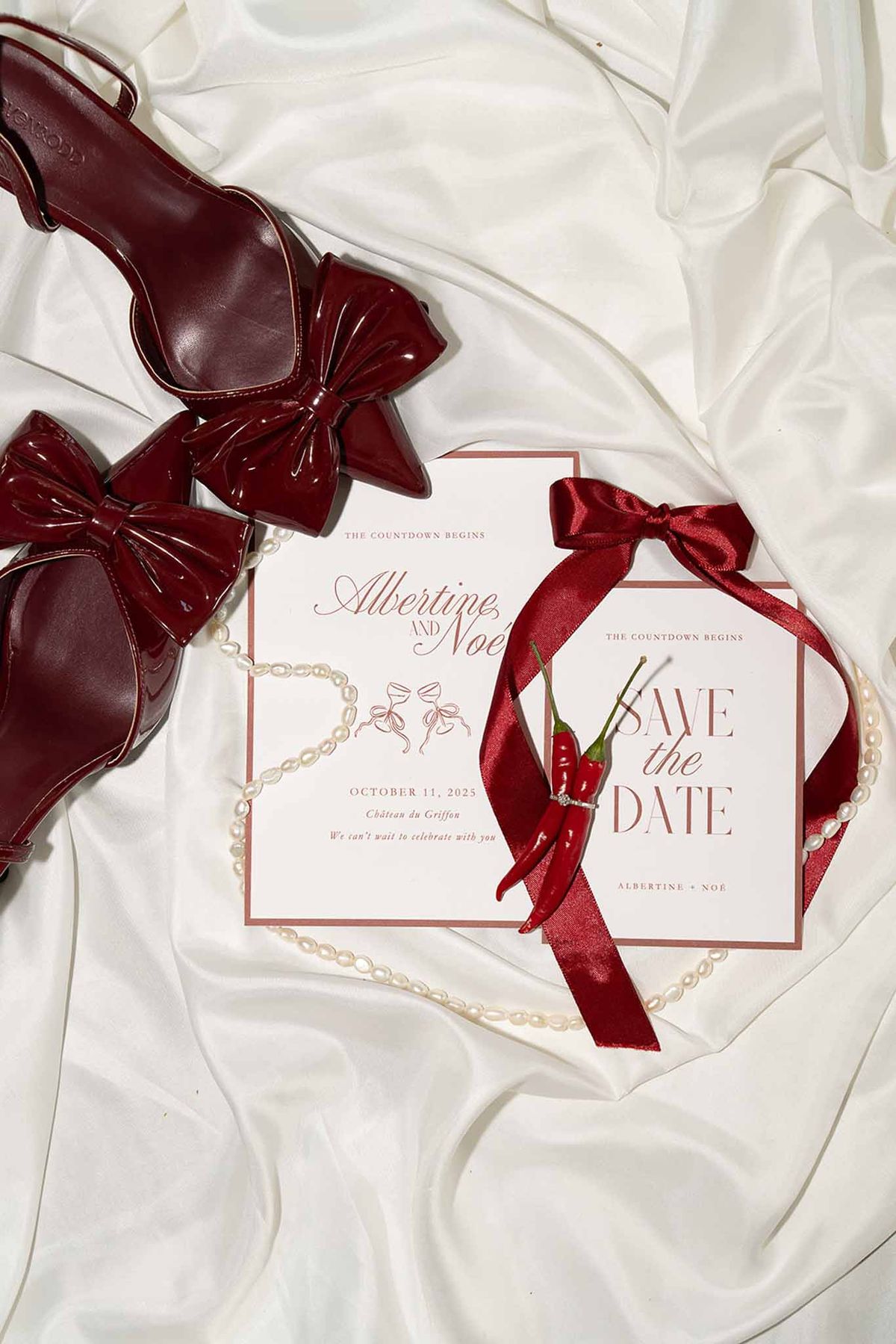 Flatlay with white and red themed invitation shoes ribbon and chilli