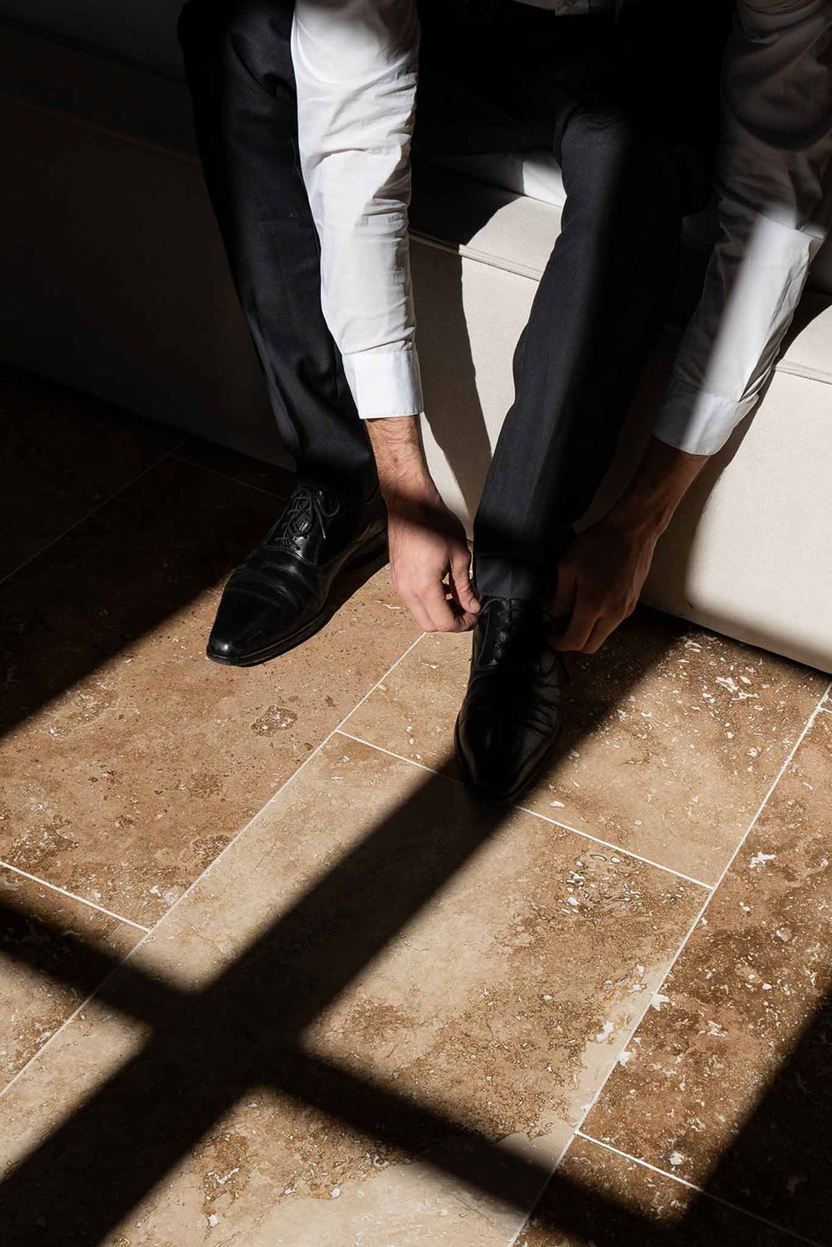 Groom putting on shoes in sunlight at Château du Griffon