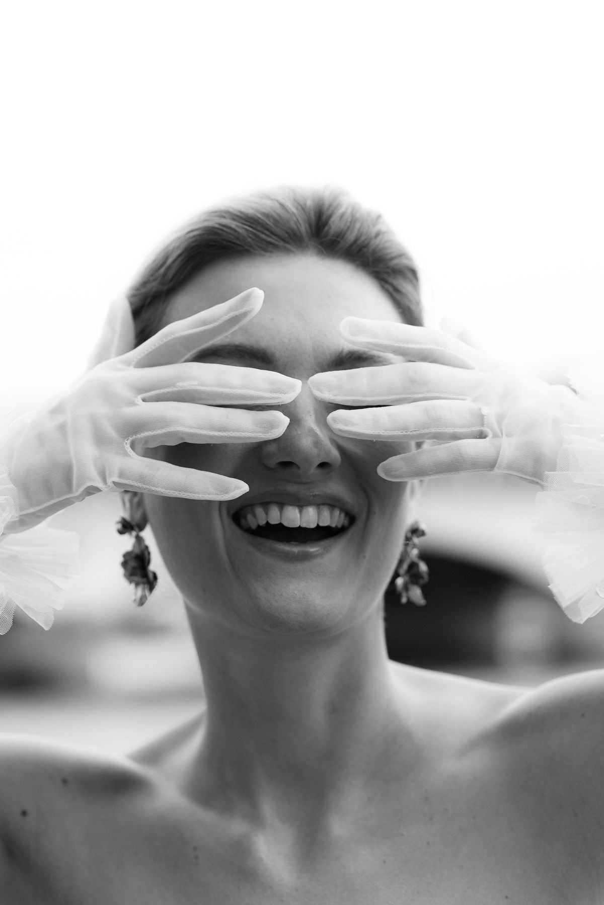 Bride laughing behind satin gloves in a black and white portrait