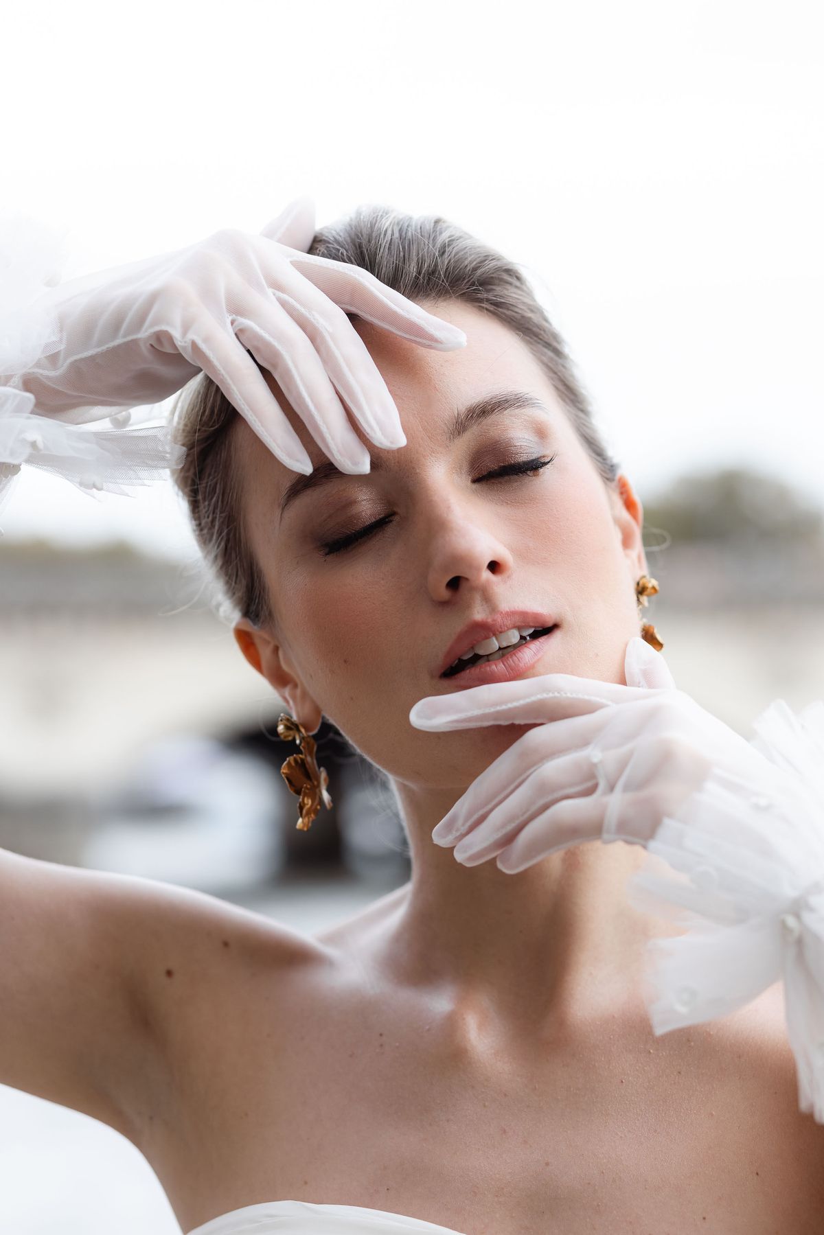 Close portrait of the bride with gold earrings and satin gloves
