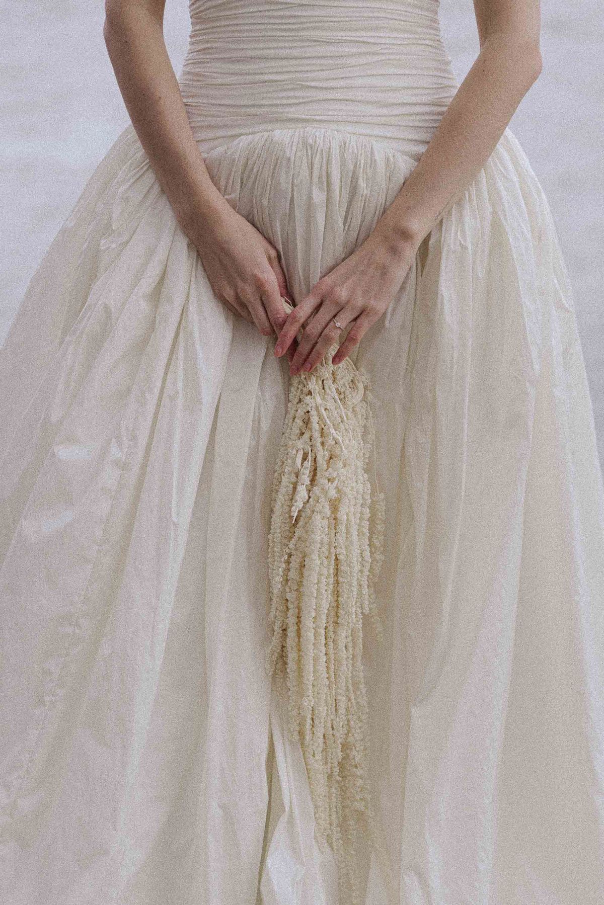 Bride's hands and gold ring resting on a textured gown
