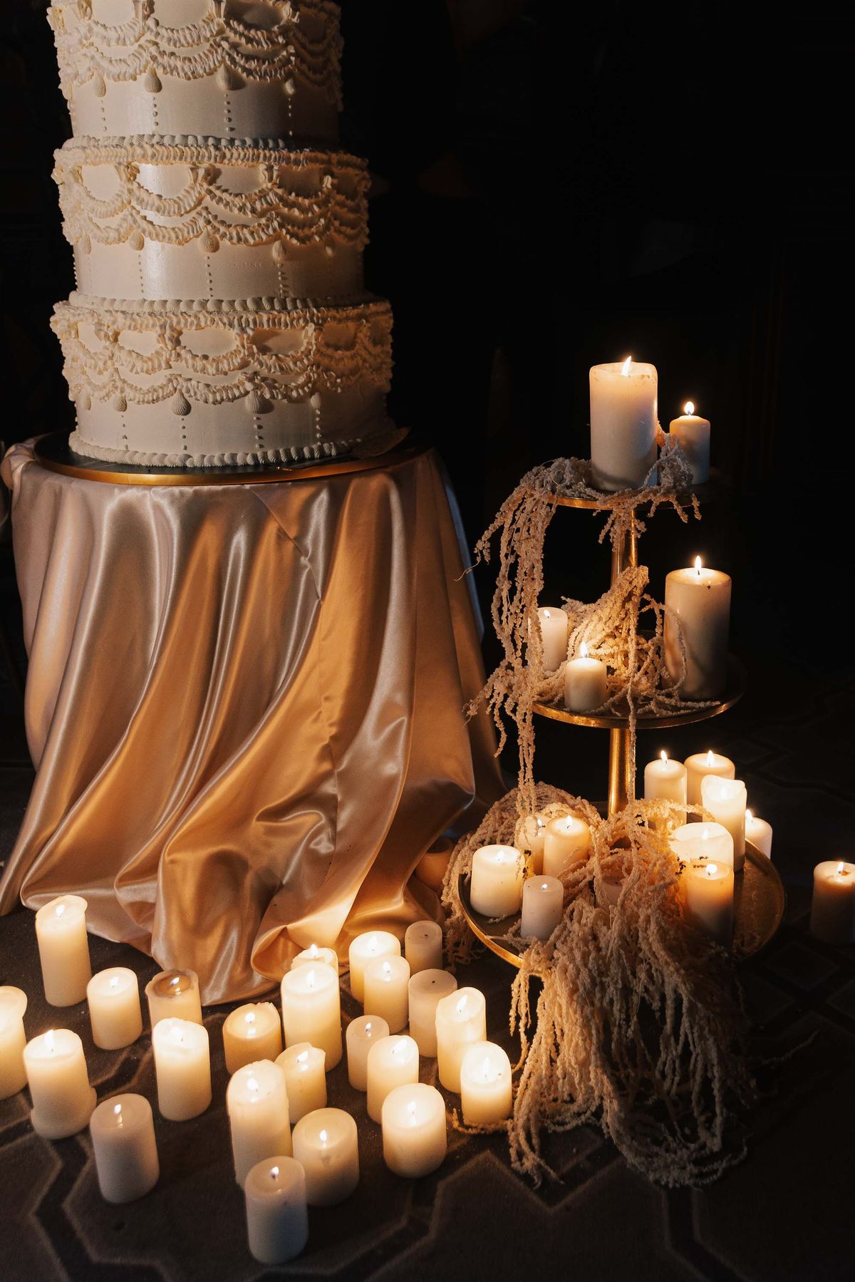 Candles and gold satin surrounding the tiered wedding cake