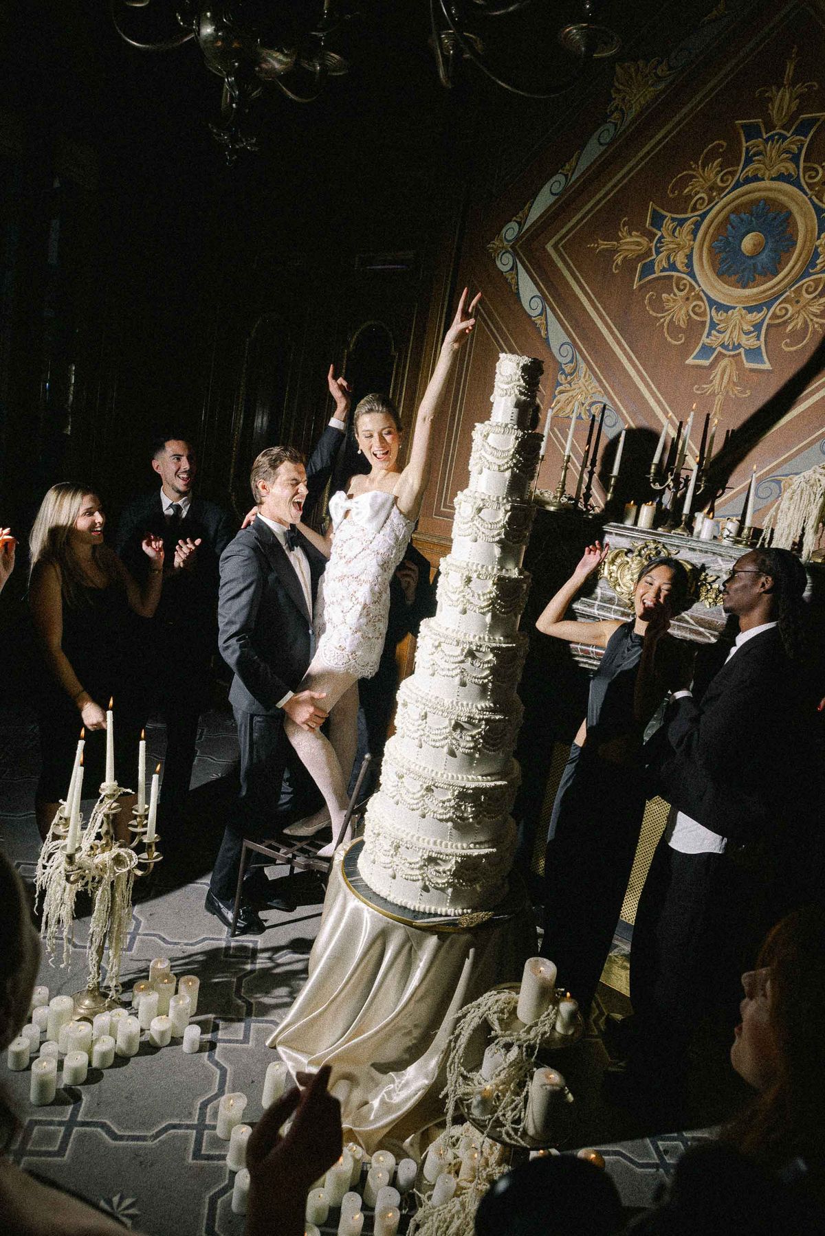 Couple and guests around the tiered cake at the candlelit reception