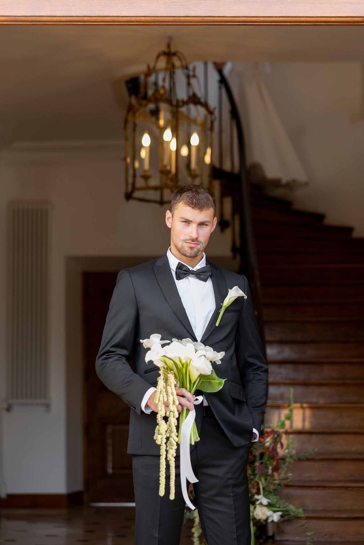 Groom holding bride's bouquet in château entrance hall at Château Comtesse Lafond