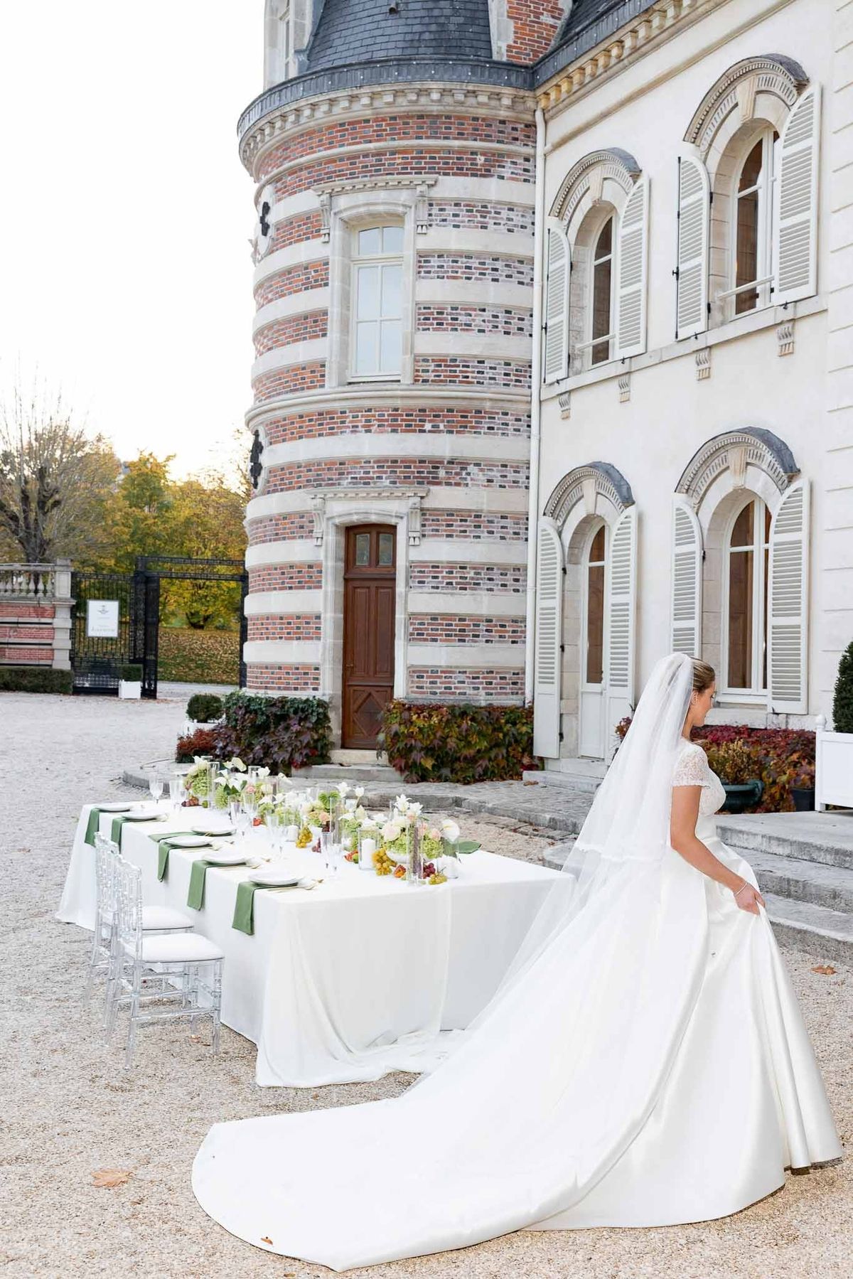 Bride with veil walking past red brick turret at Château Comtesse Lafond