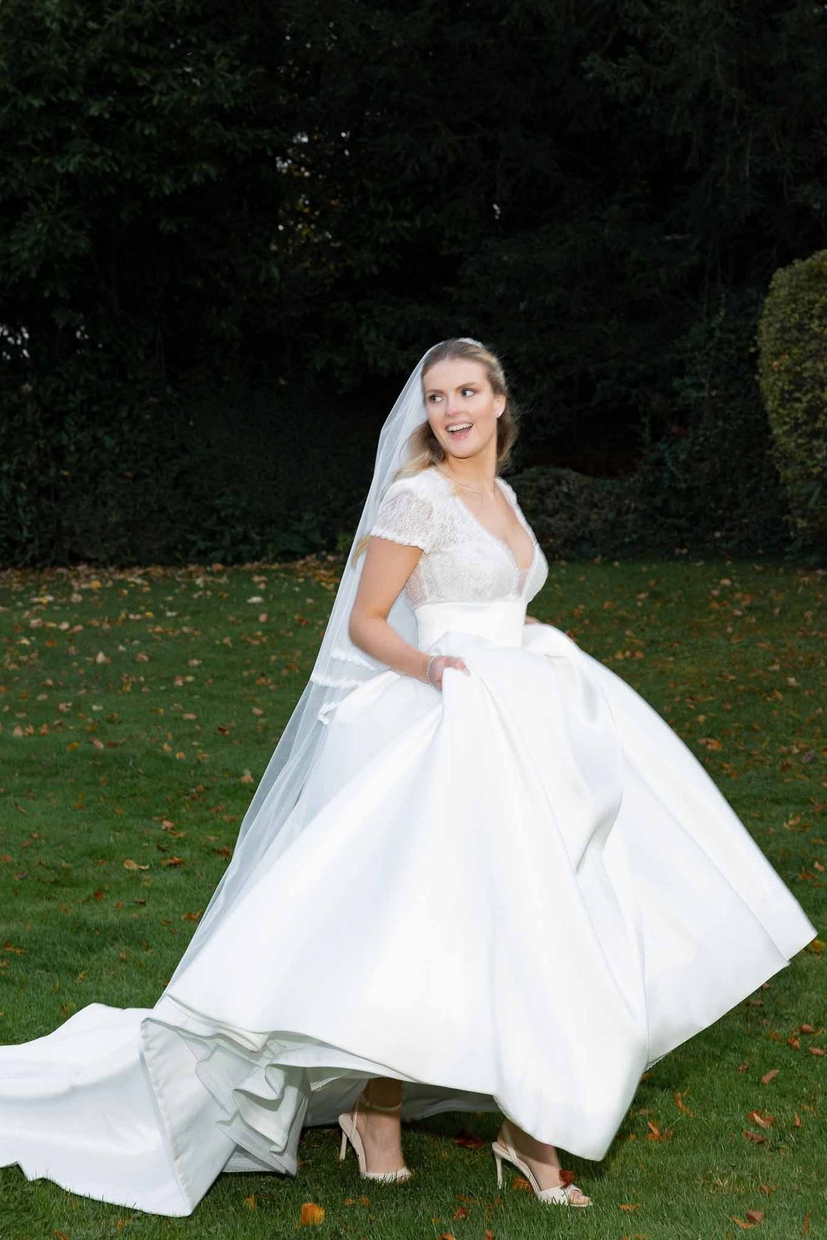 Bride lifting ball gown skirt playfully on autumn lawn at Château Comtesse Lafond