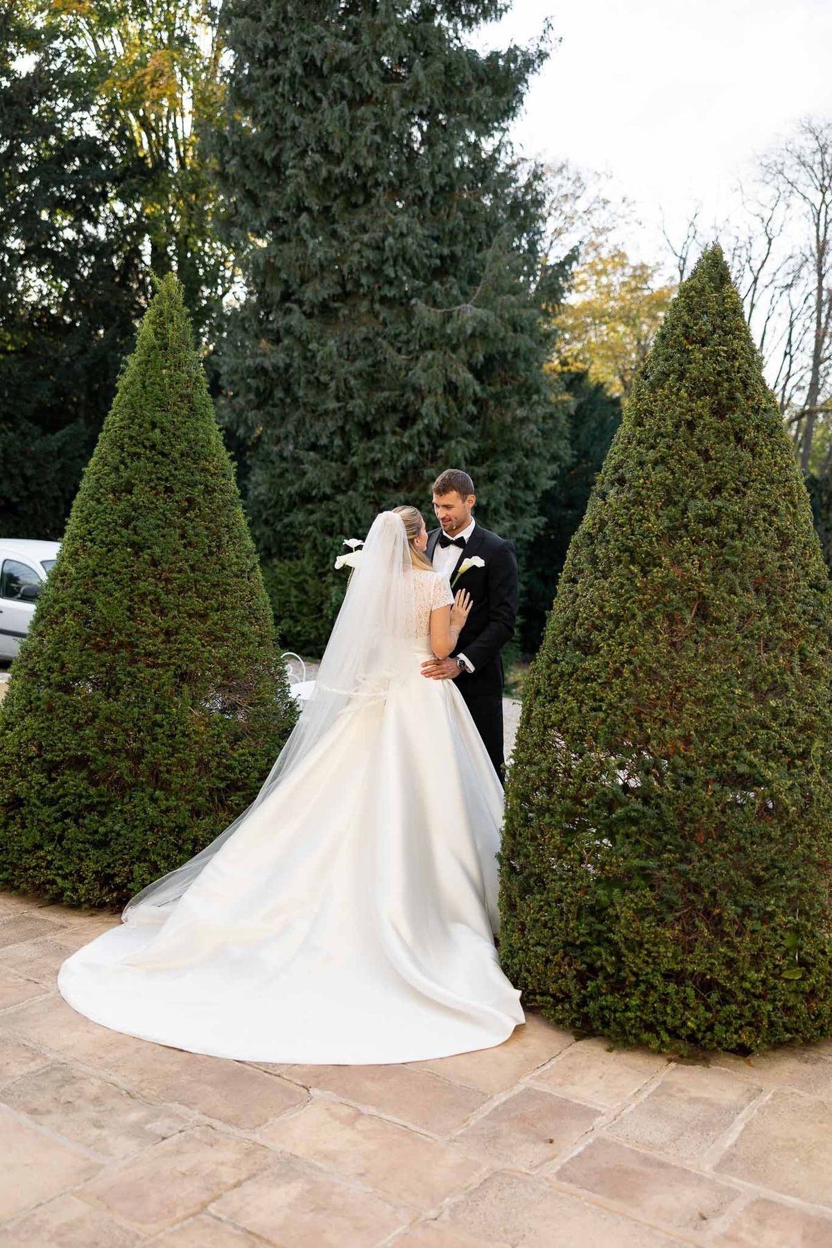 Bride and groom embracing between conical topiaries at Château Comtesse Lafond