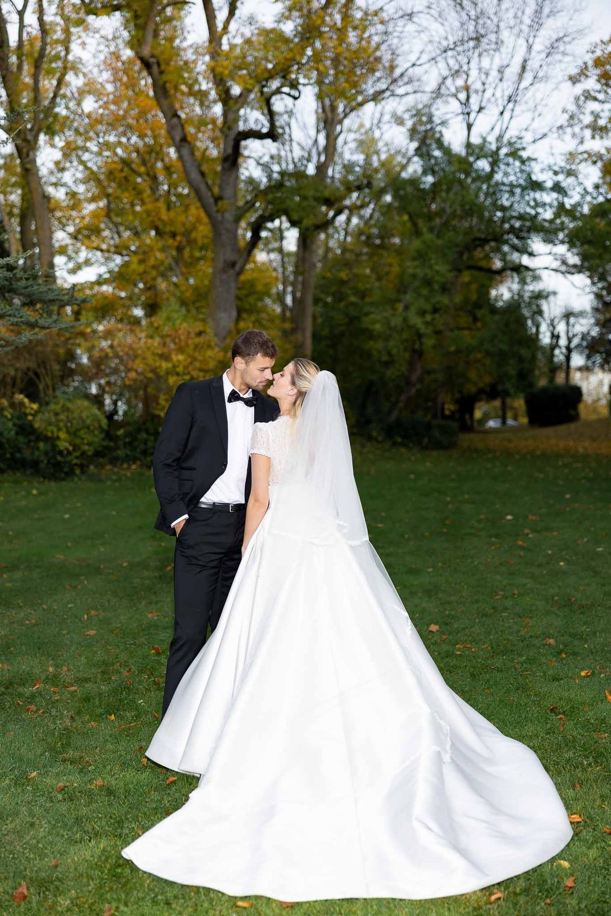 Couple kissing on autumn lawn beneath golden trees at Château Comtesse Lafond