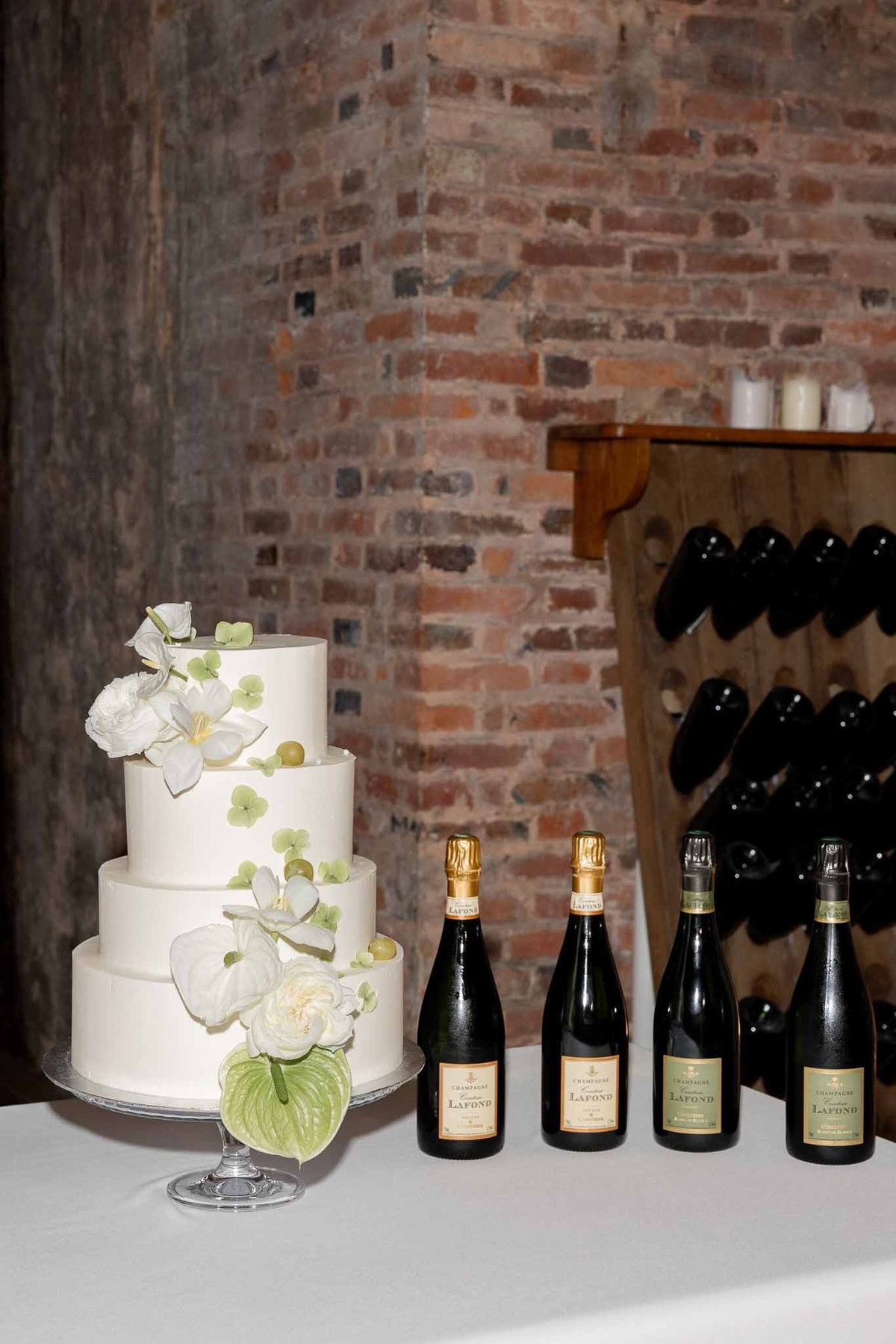 Three-tier wedding cake with orchids beside Comtesse Lafond champagne bottles in cellar