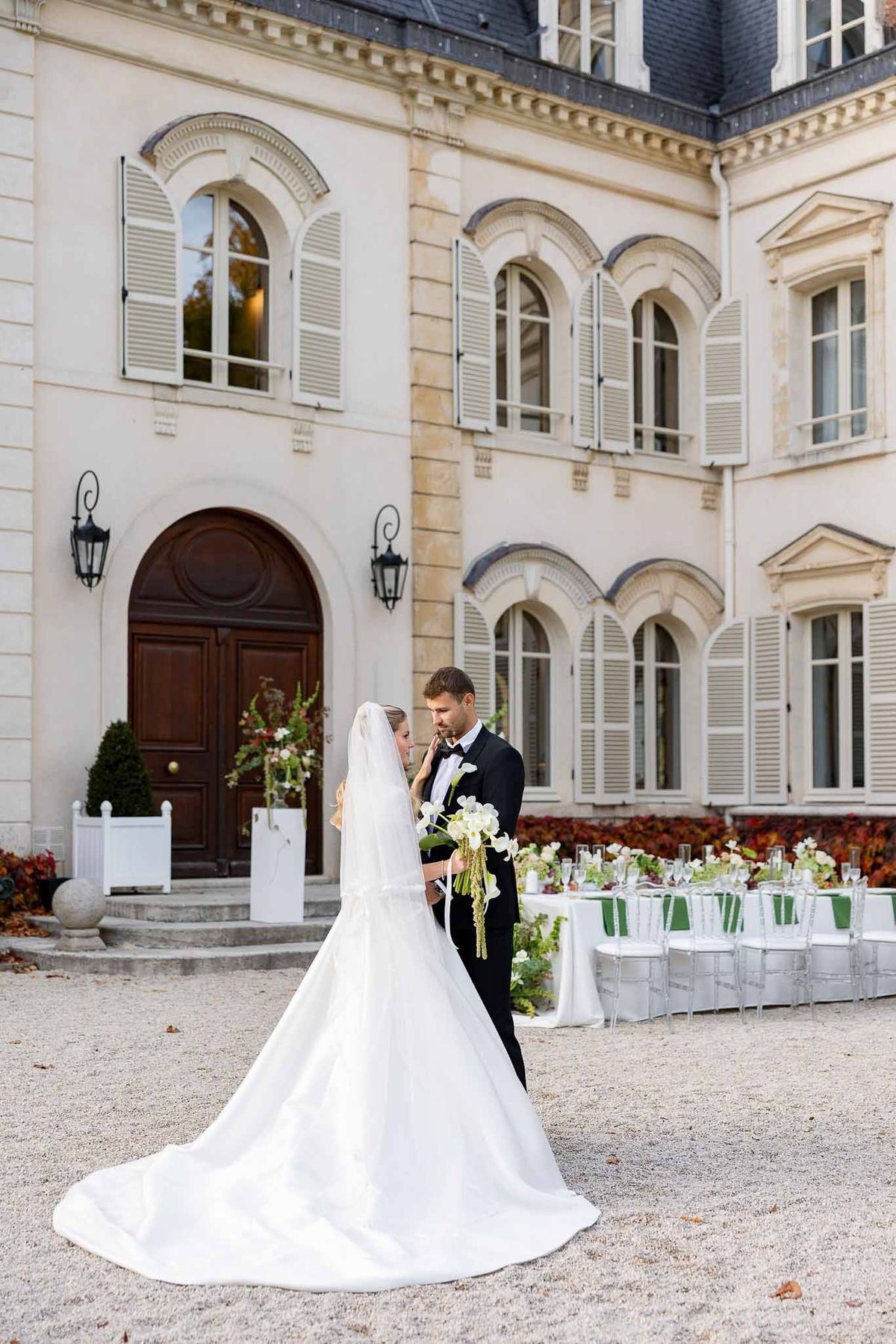 Groom kissing bride's hand in courtyard with reception tables at Château Comtesse Lafond