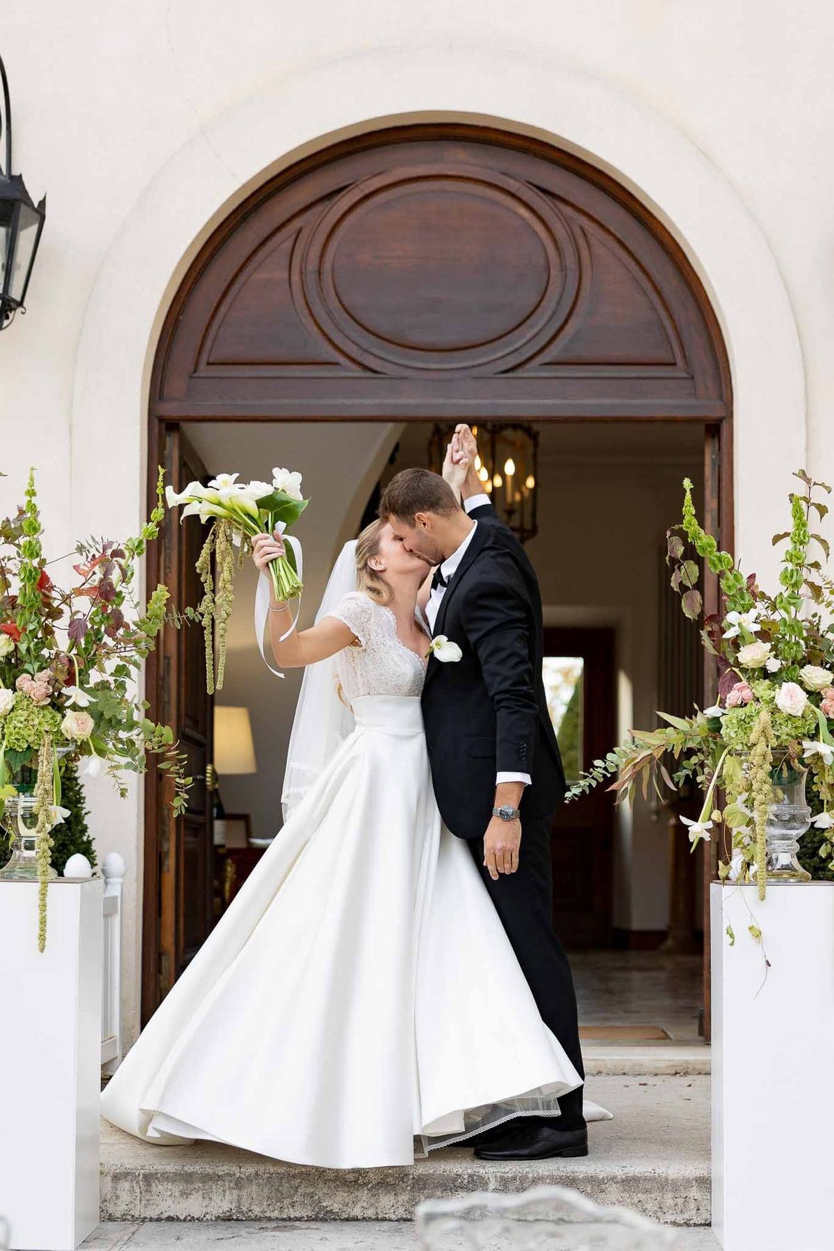 Couple kissing in arched doorway with floral arrangements at Château Comtesse Lafond