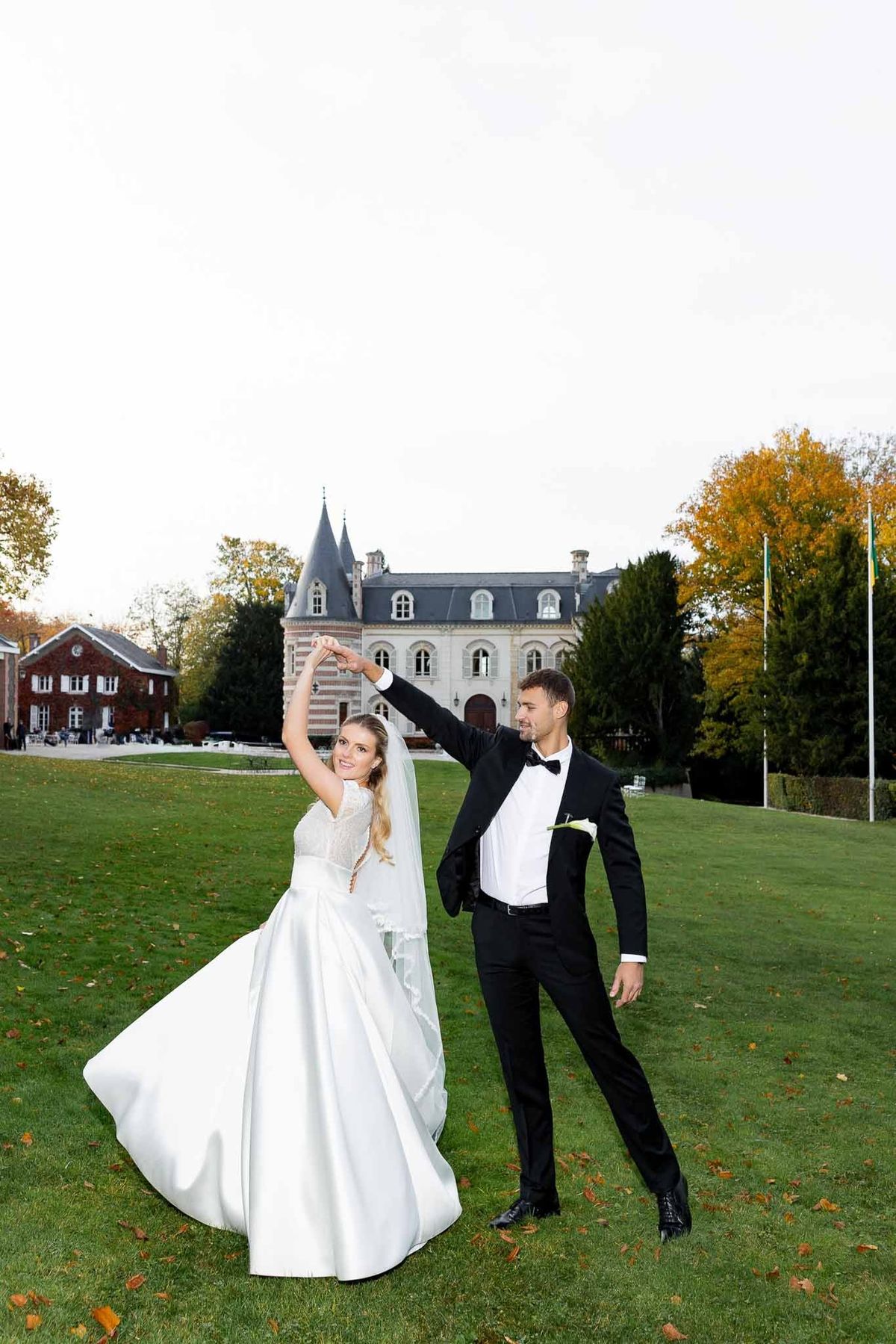Groom twirling bride on lawn with château turrets behind at Château Comtesse Lafond