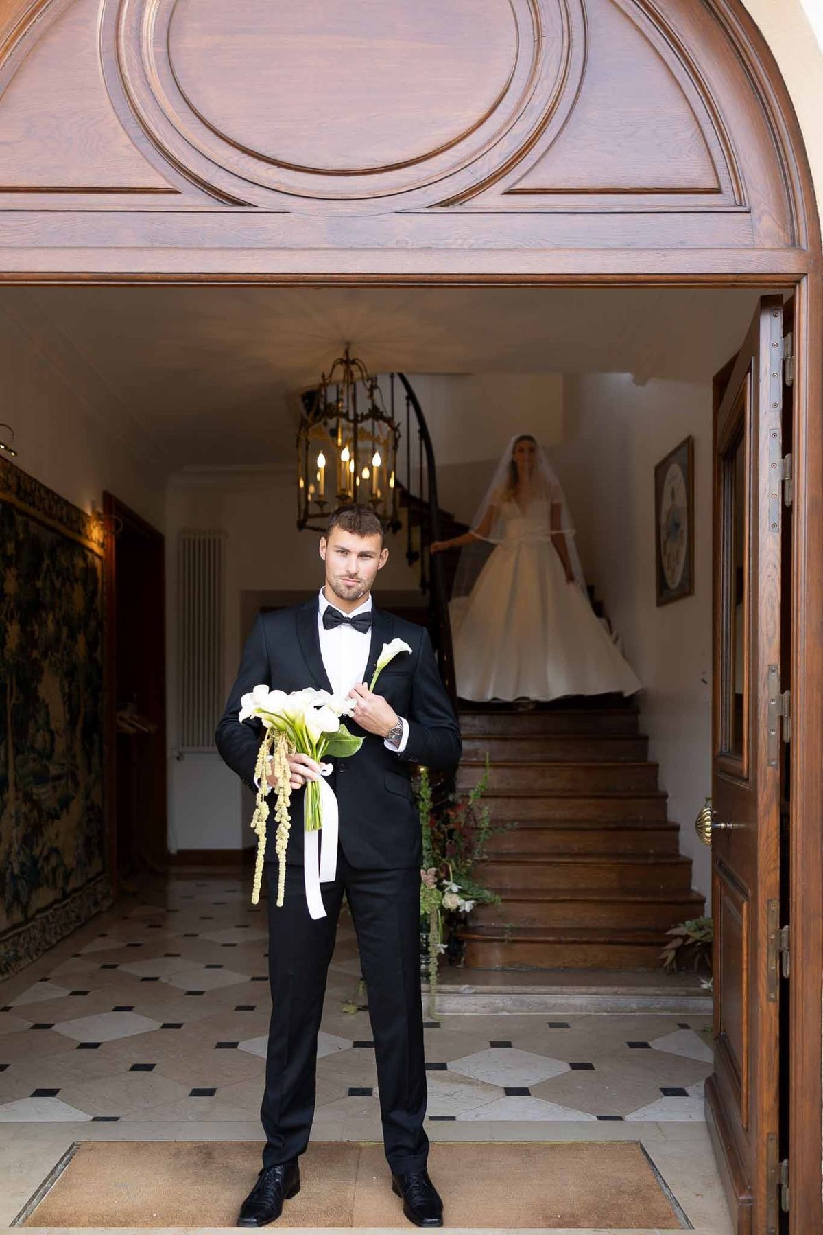 Groom waiting with bouquet as bride descends staircase for first look at Château Comtesse Lafond