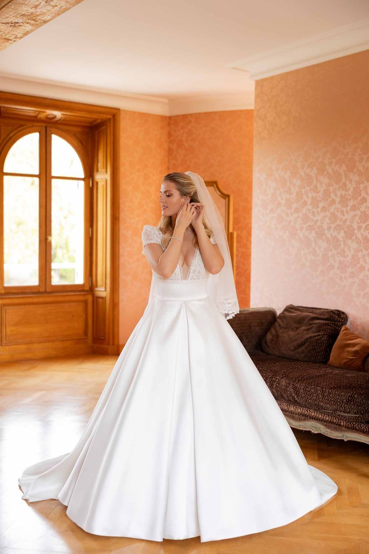 Bride putting on pearl earring in rose-papered room at Château Comtesse Lafond
