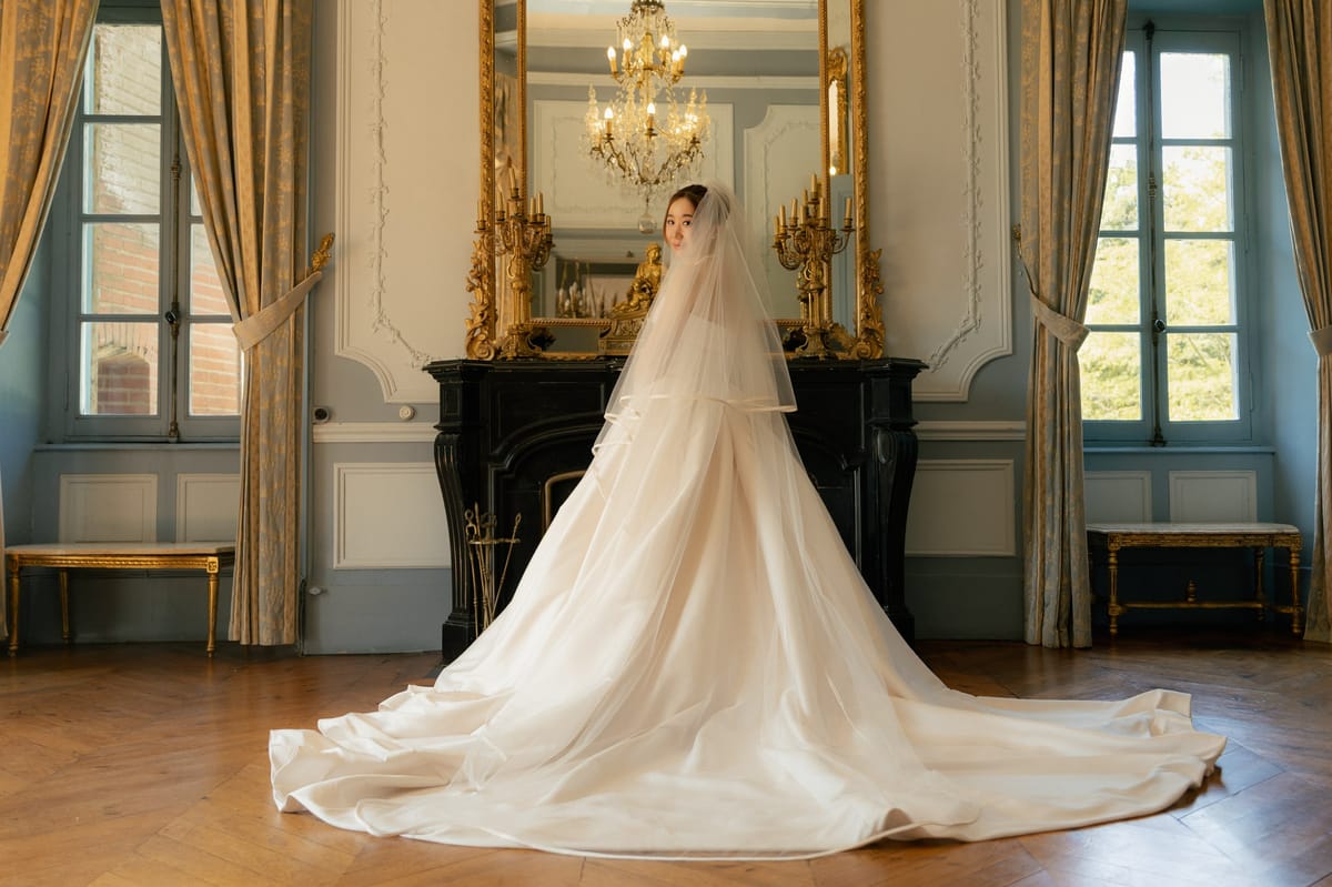 Bride with cathedral train and veil in blue-grey paneled salon with gilt candelabras and marble fireplace