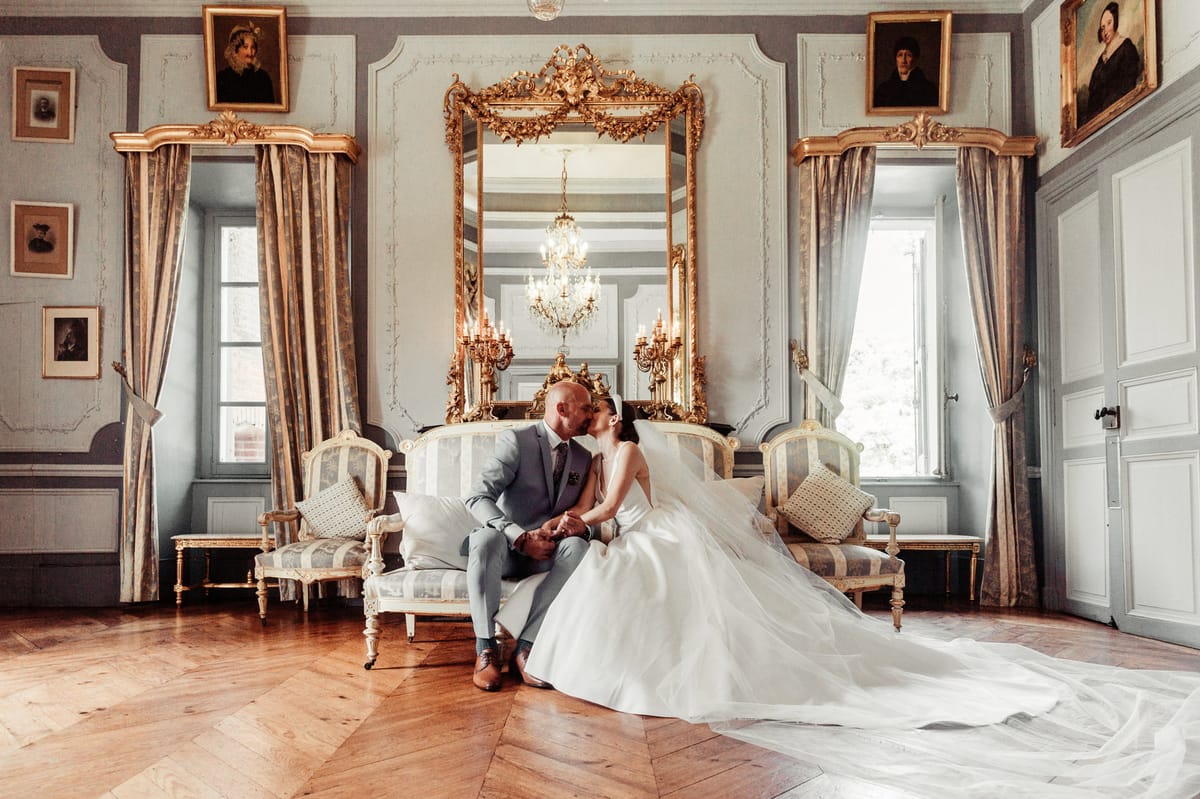 Couple kissing on gilded sofa in chateau salon with boiserie panelling and rococo mirror