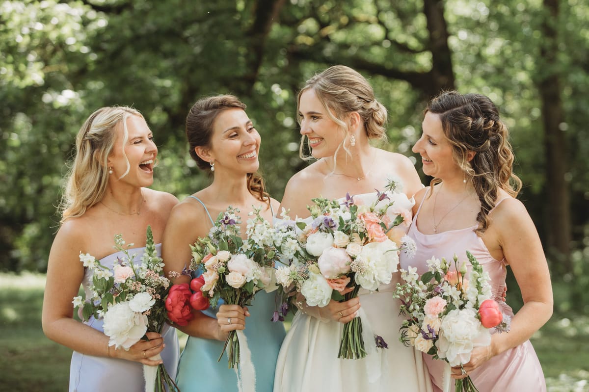 Bride with three bridesmaids in mismatched pastel slip dresses holding garden-style bouquets
