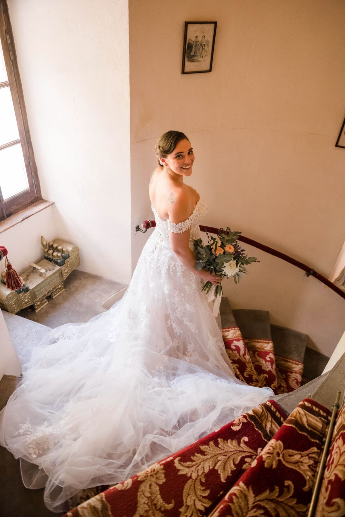 Bride on chateau staircase looking over shoulder with lace train cascading down carpeted steps