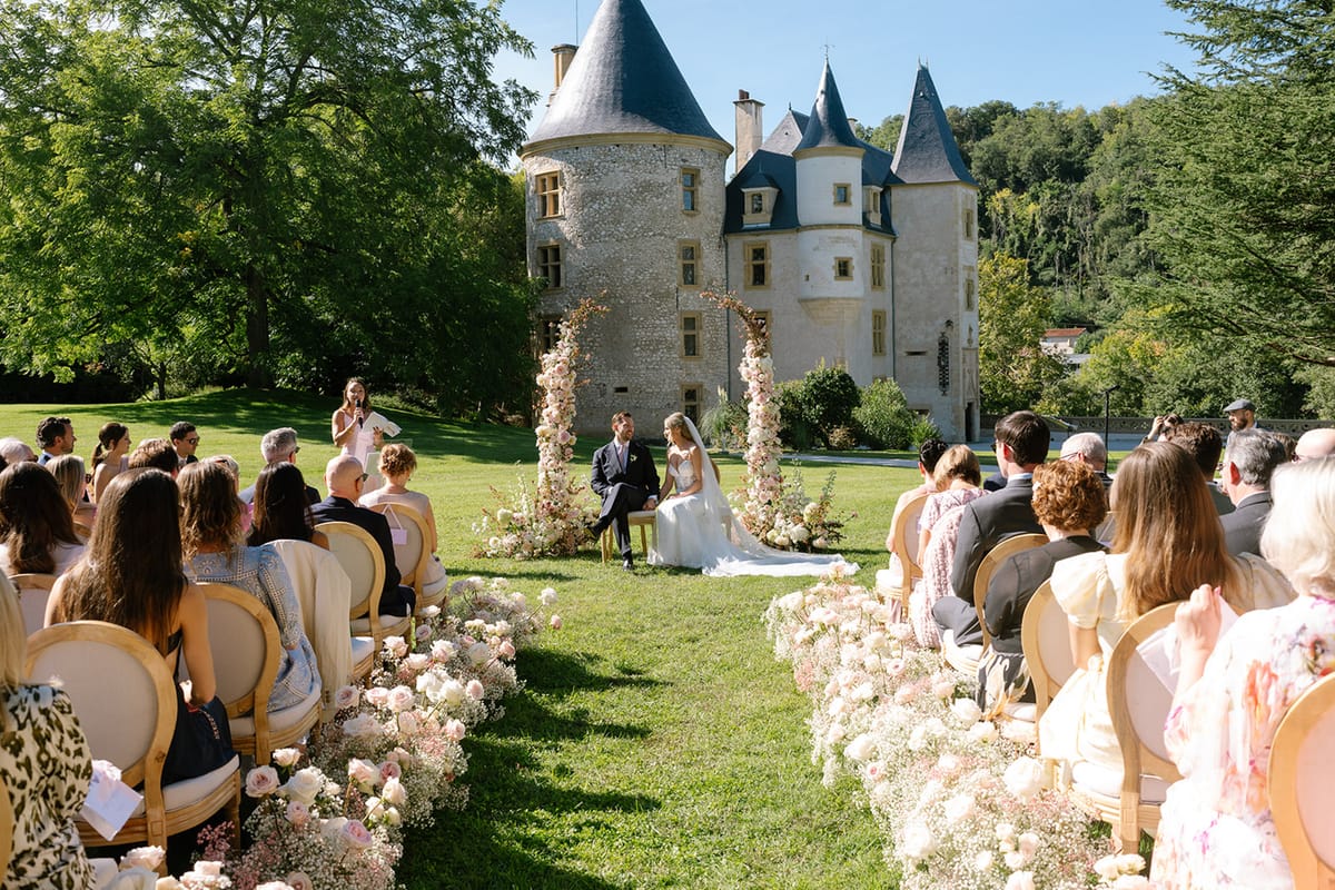 Outdoor wedding ceremony on chateau lawn with floral columns, gold chairs, and stone towers in background