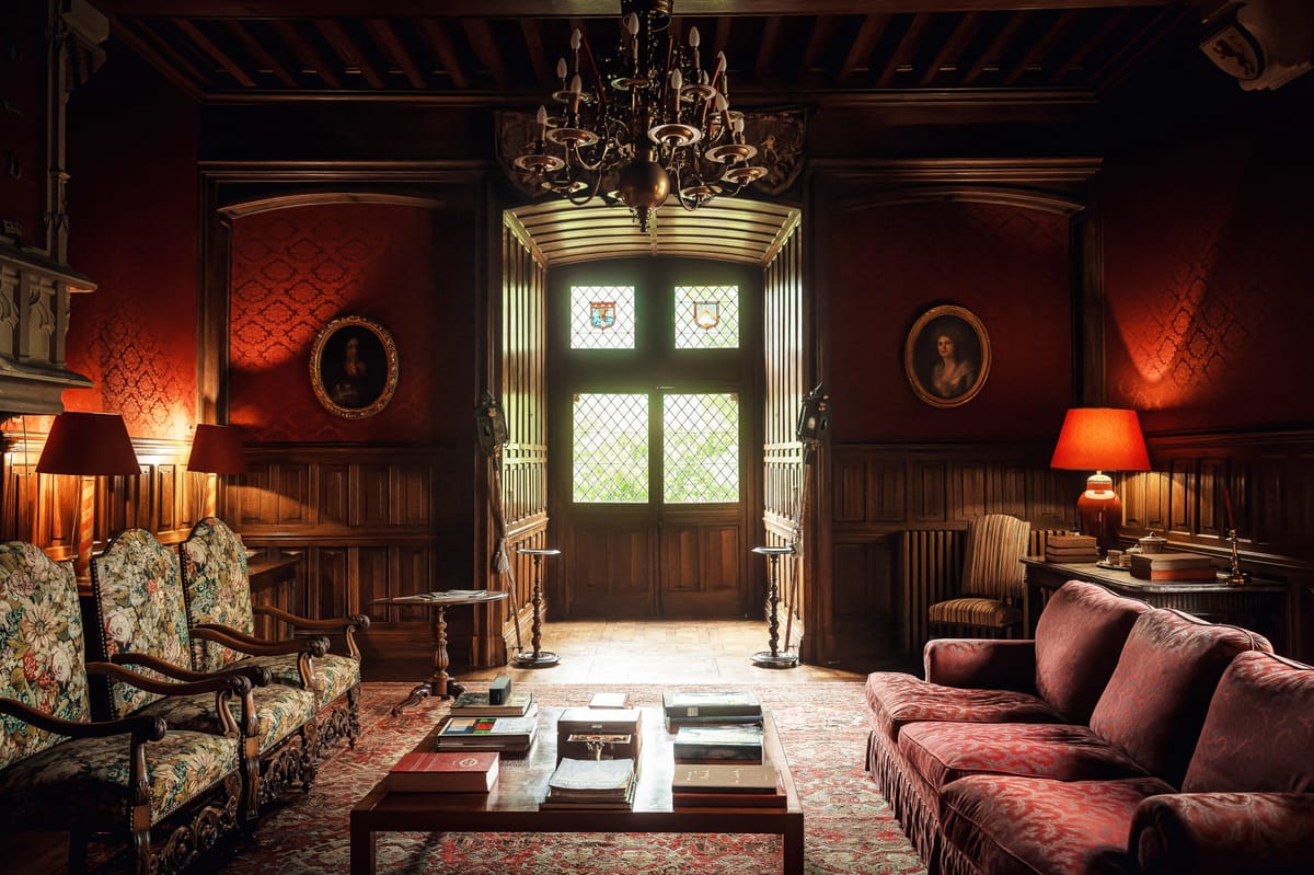 Chateau salon with crimson damask walls, burgundy velvet sofa, wrought-iron chandelier, and gilt portraits