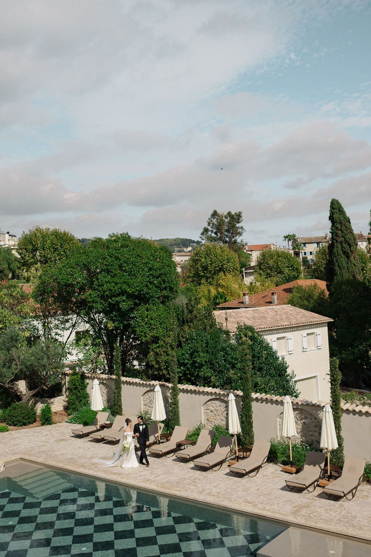 Drone shot of bride and groom walking poolside at French wedding venue