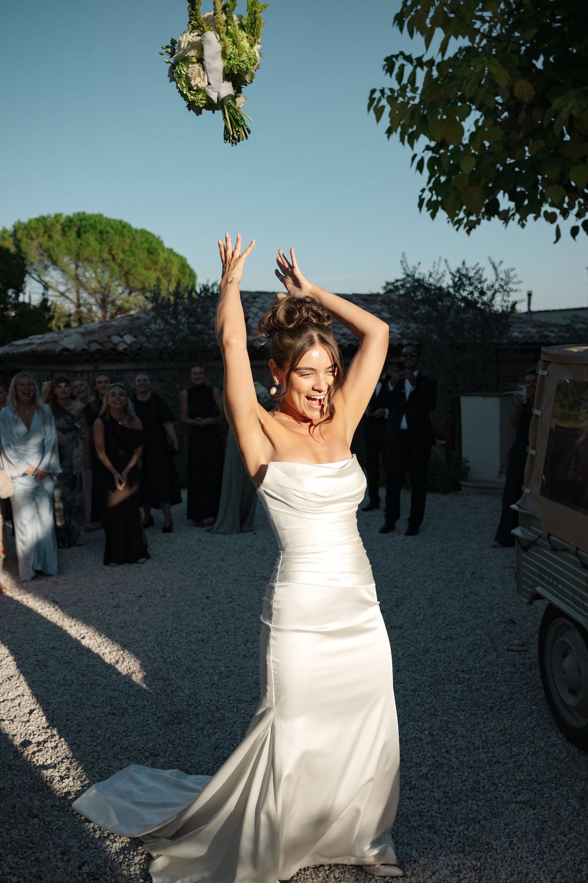 Bride tossing white bouquet during reception celebration in courtyard