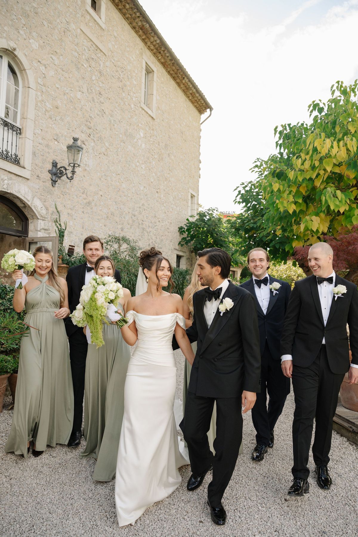 Wedding party walking along stone chateau wall in candid portrait