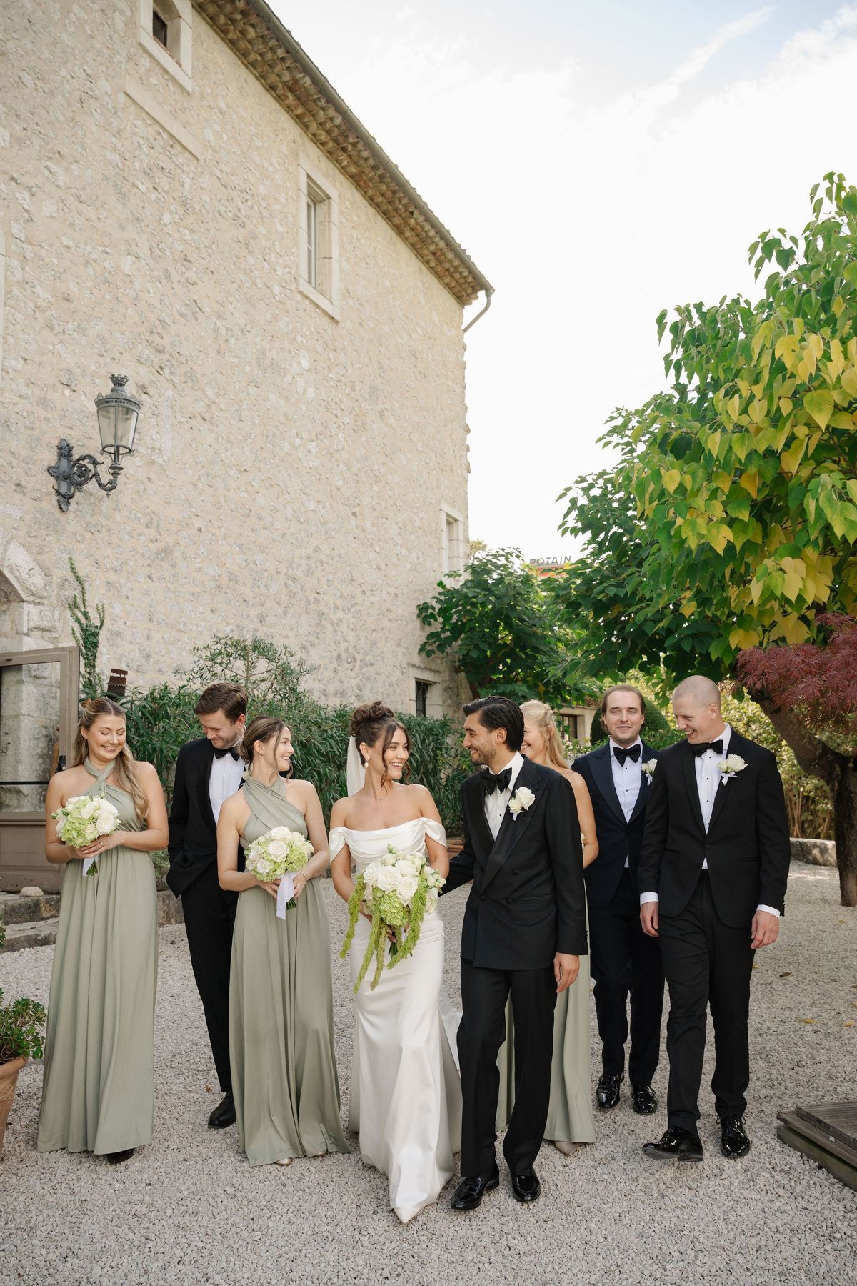Bride and groom walking with wedding party beside chateau garden wall