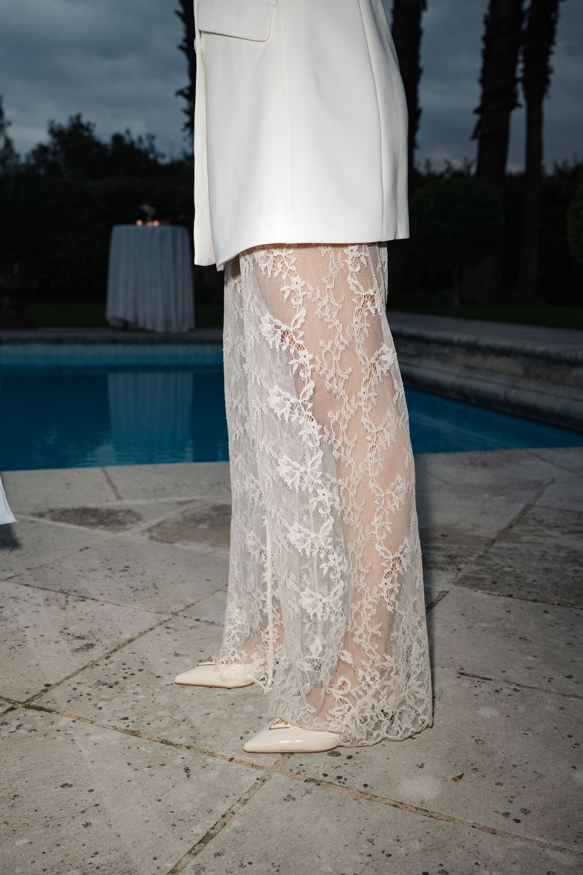 Detail of white lace skirt and pointed bridal shoes beside venue pool