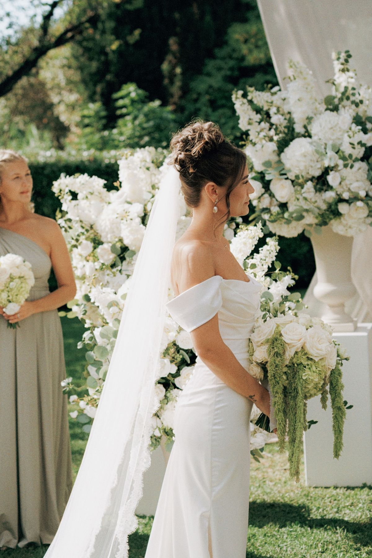 Side profile of bride in off-shoulder gown with veil at floral altar