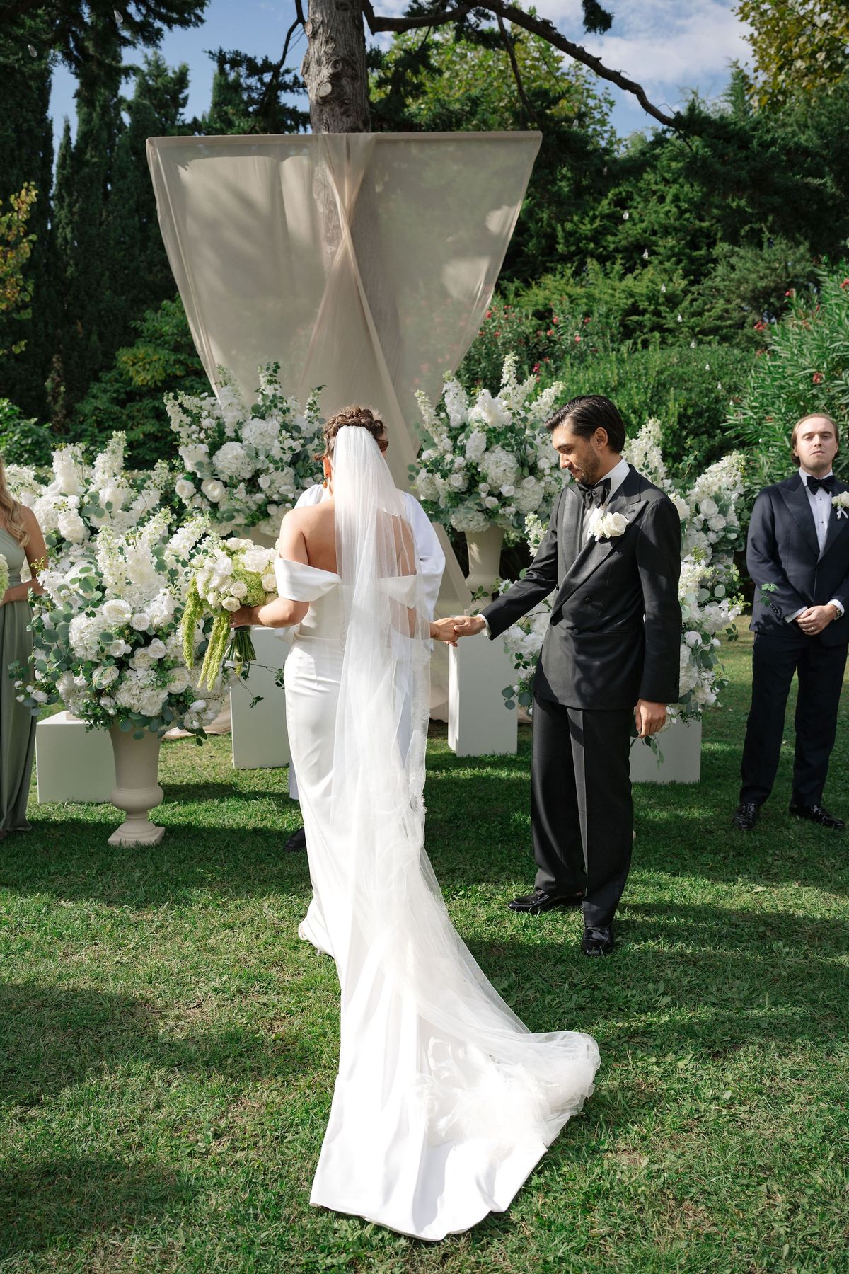 Couple holding hands at outdoor ceremony altar with draped fabric arch