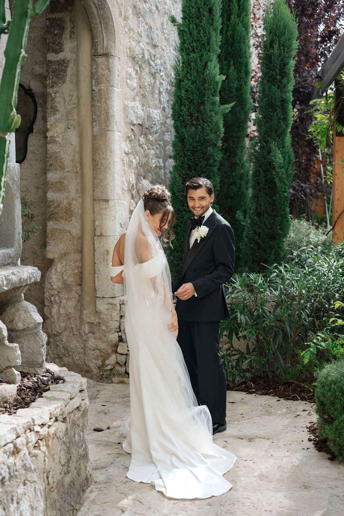 Bride and groom share a quiet laugh beside stone archway in garden