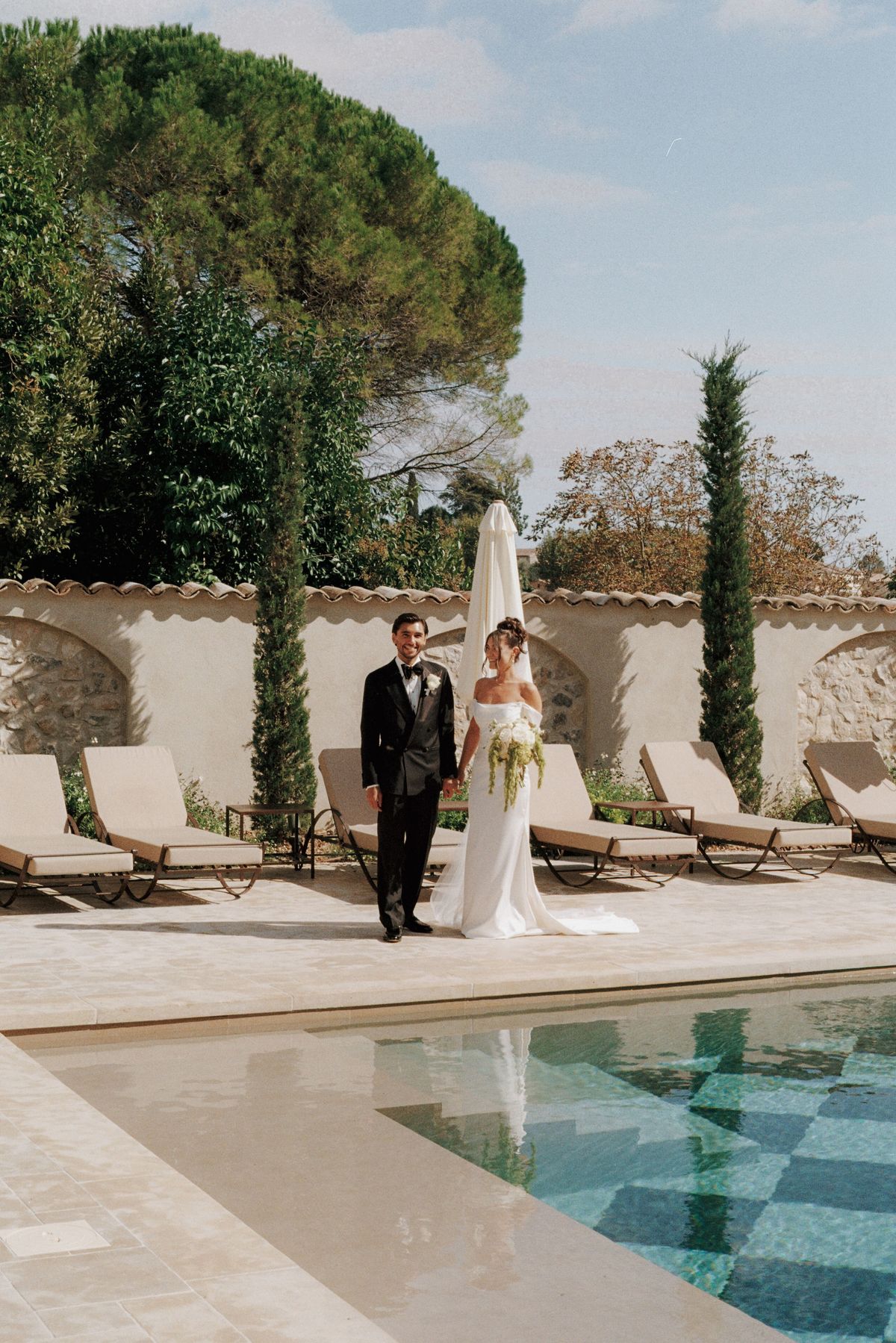 Couple holding hands beside checkerboard pool framed by cypress trees