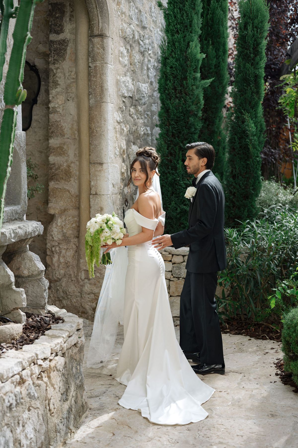 Bride and groom pausing by stone arch during garden couple portraits
